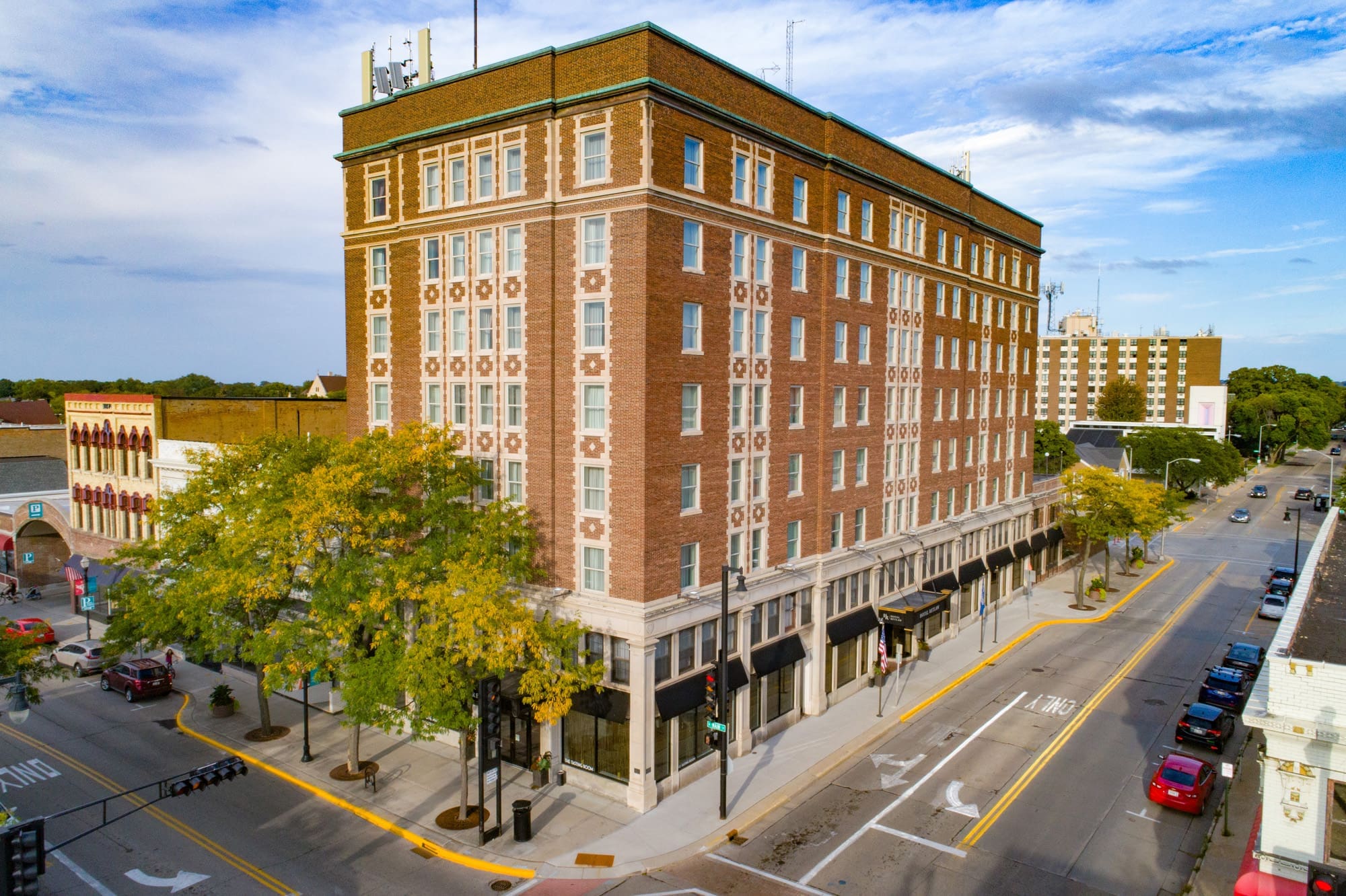 Commercial real estate photo of a large, historic brick building with green roof trim at a downtown corner under a clear blue sky. Commercial real estate photo of a large, historic brick building with green roof trim at a downtown corner under a clear blue sky.