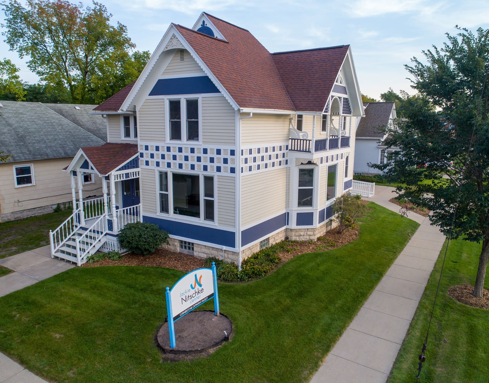Residential property exterior featuring two-story home with blue trim, manicured lawn, sidewalks; sign out front reads The NestHue.