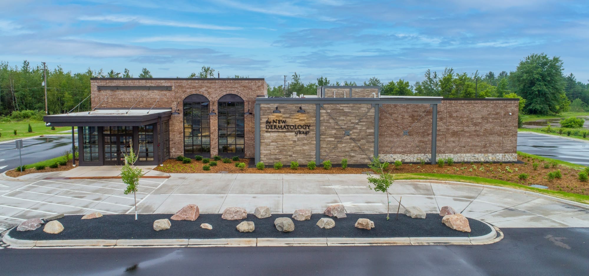 Commercial property photo of a modern brick medical office, ATMN Dermatology, with large windows, arched entry, and vacant parking lot.