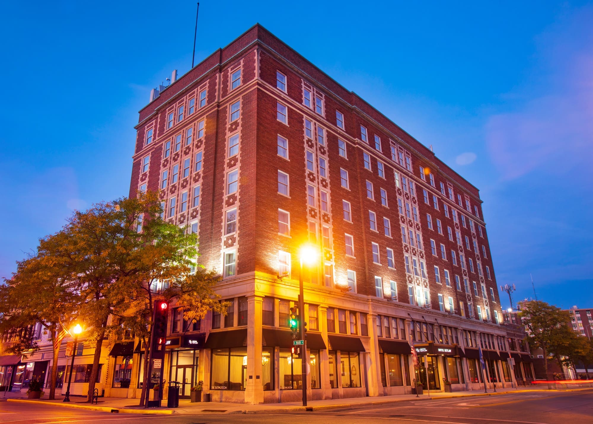 Commercial multi-story brick property with street-level retail spaces, photographed at dusk on a quiet city corner, well-lit for real estate.