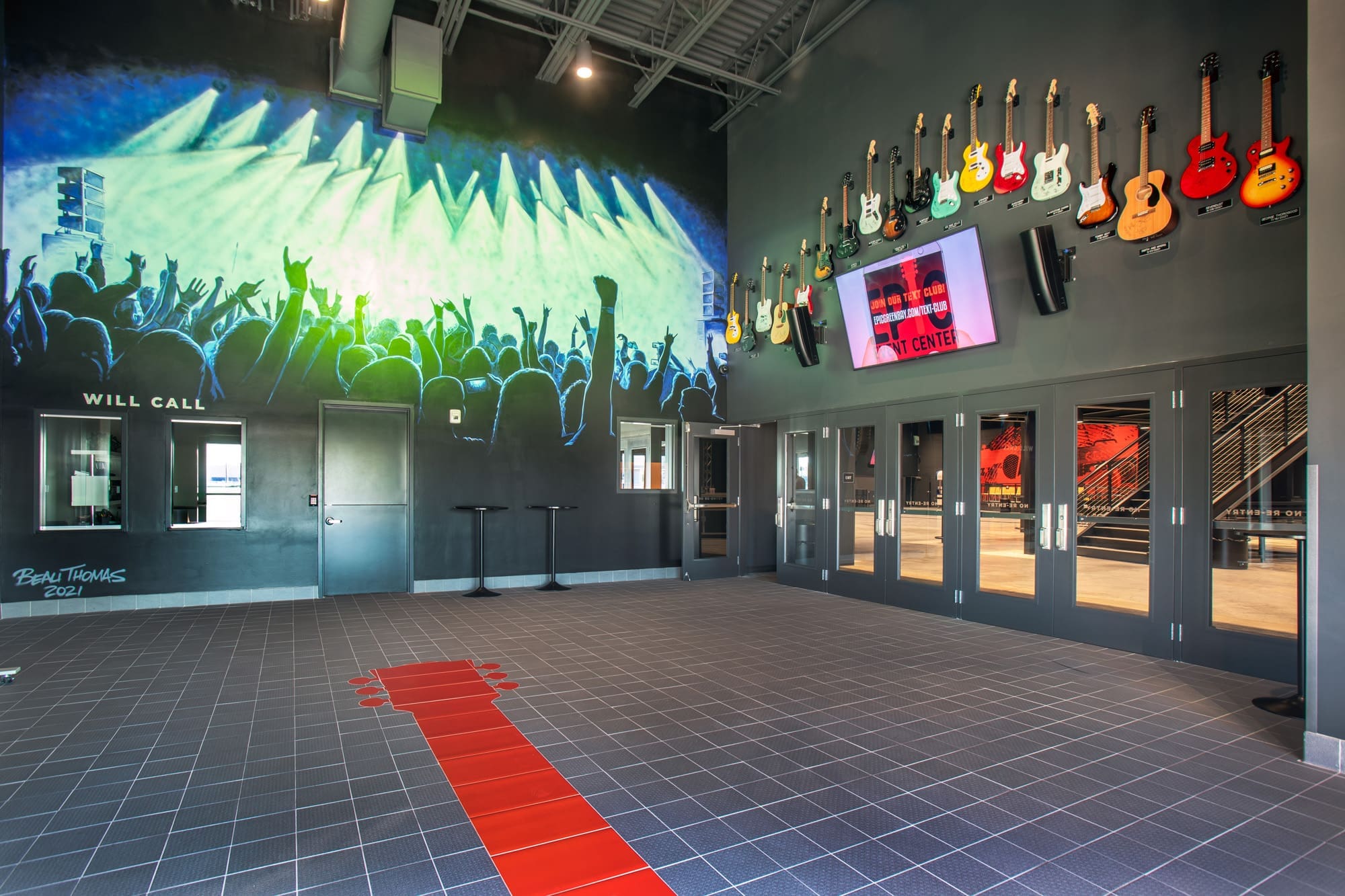 Commercial property lobby featuring concert crowd mural, guitar wall art, digital info screens, and red guitar neck flooring design.