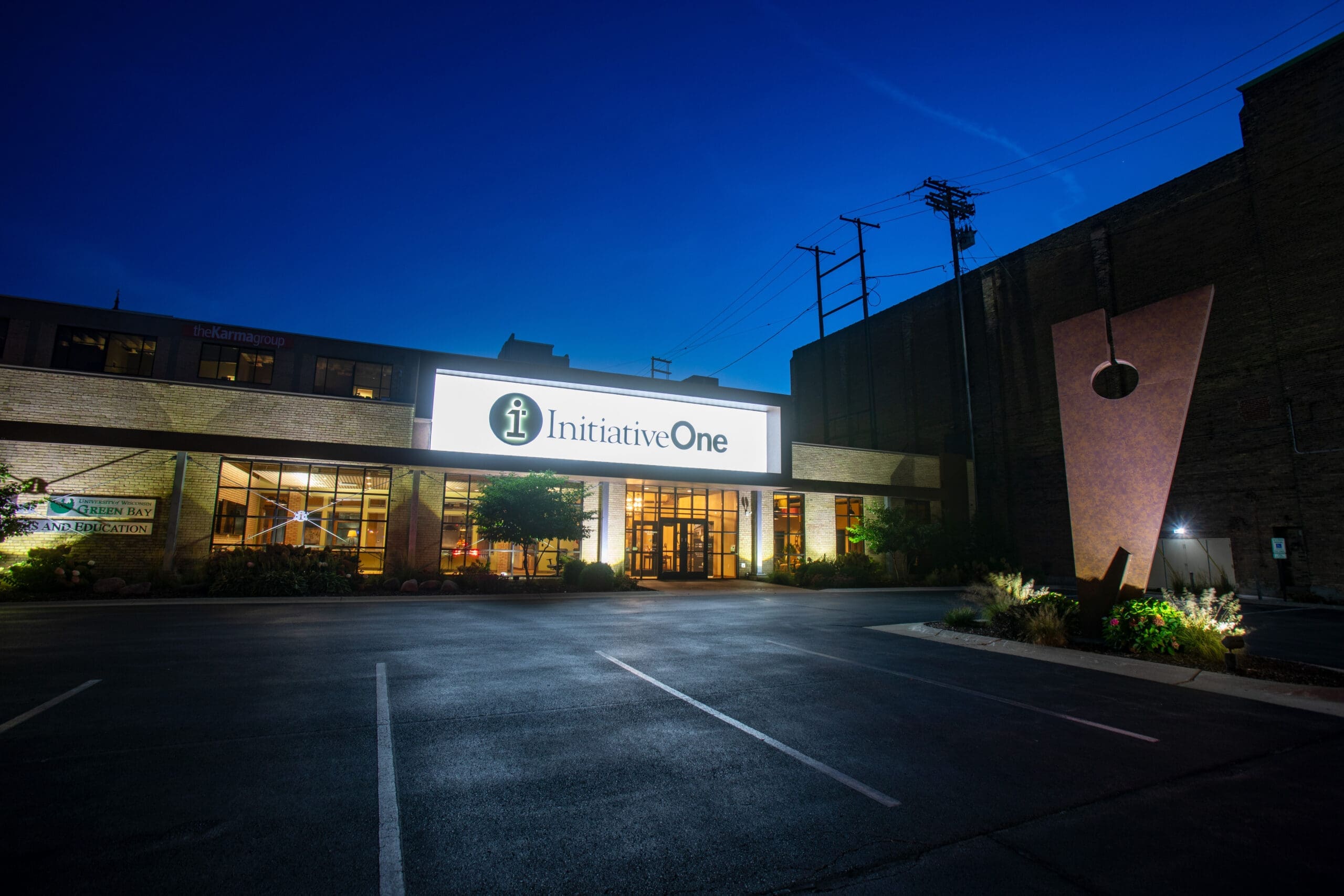 Commercial real estate photo of InitiativeOne building exterior at dusk, featuring lit signage and empty parking lot for lease appeal.