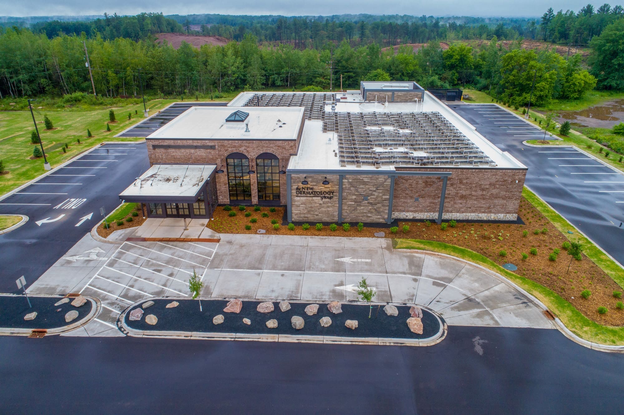 Commercial property featuring a modern building with flat white roof, ample parking, landscaped grounds, and tree-lined surroundings.