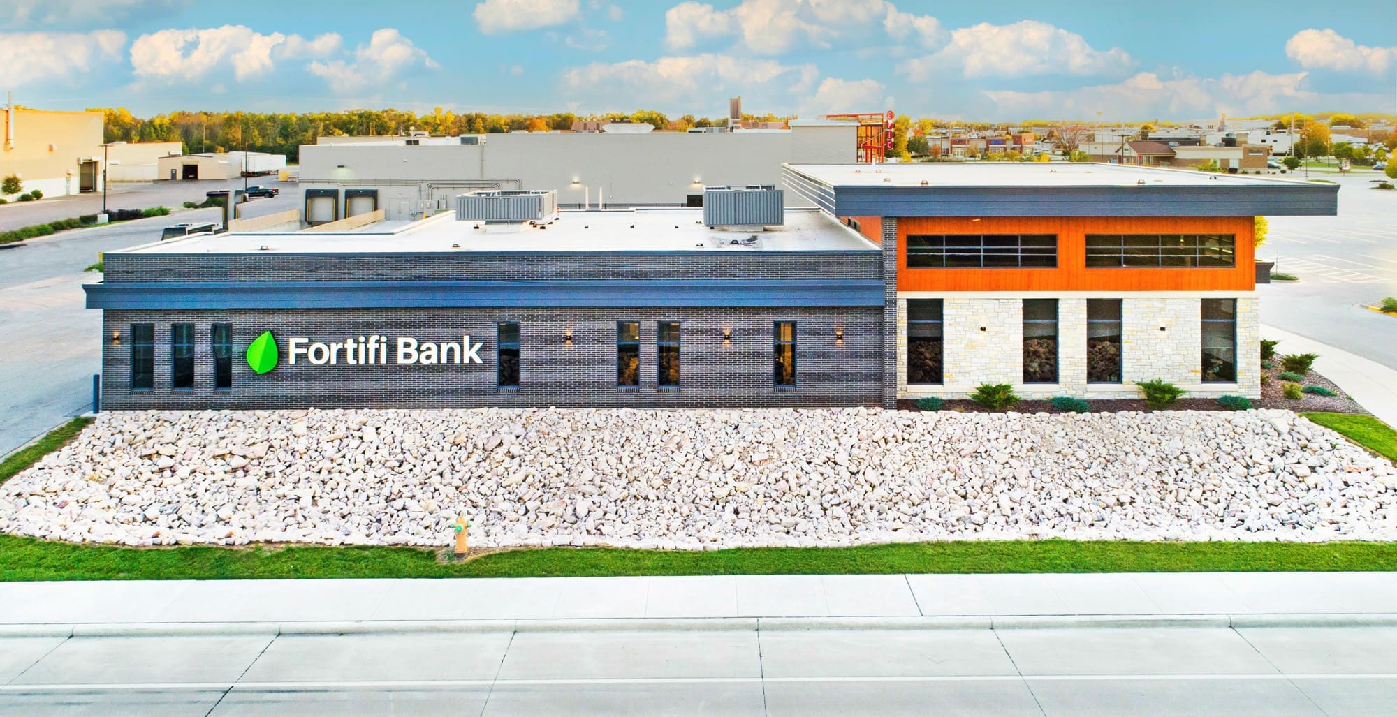 Commercial property photo of a modern Fortifi Bank, single-story, brick and stone exterior, landscaped lawn with rocks in front.