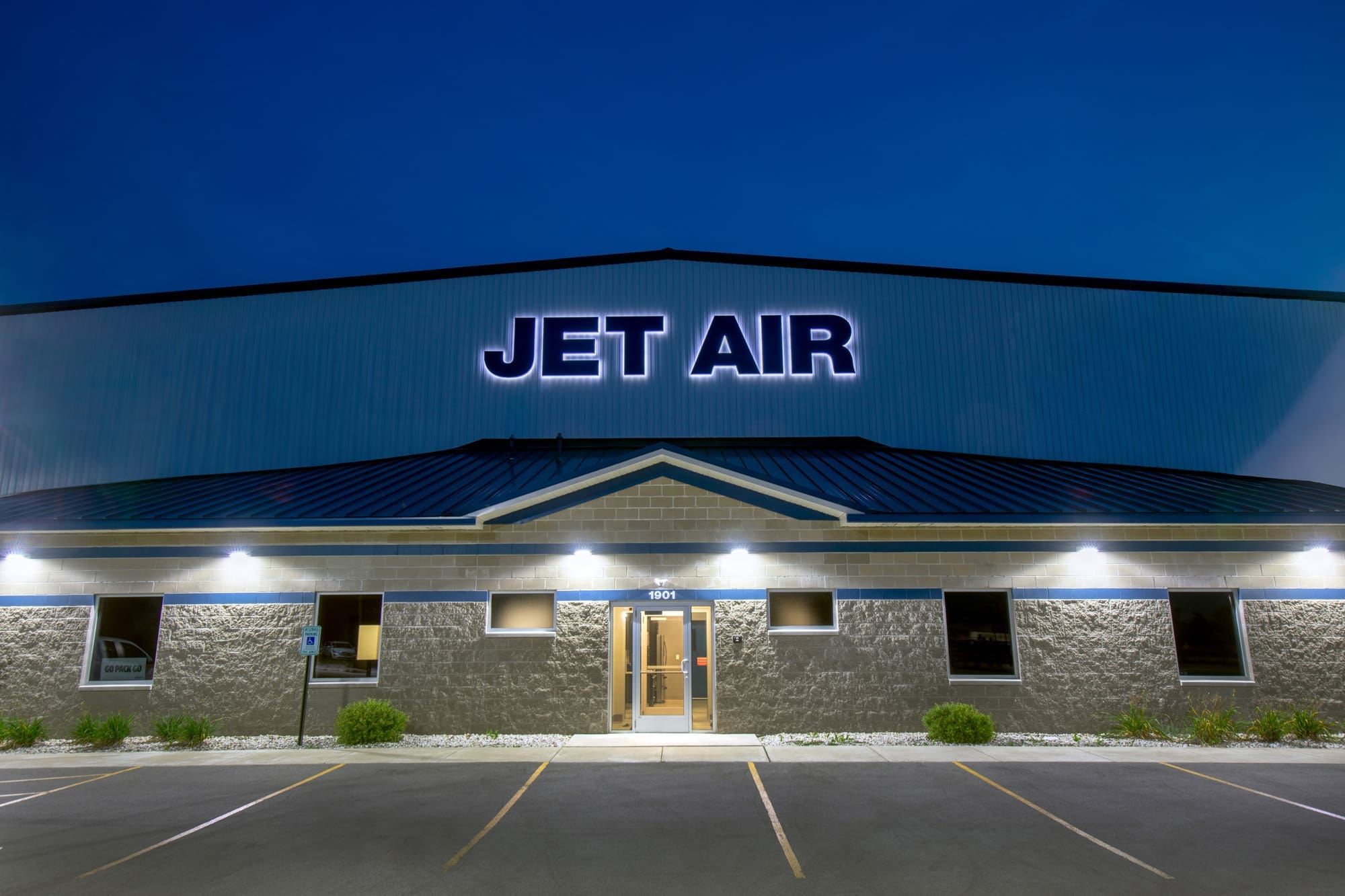 Commercial property for sale featuring JET AIR signage, dusk exterior lighting, and vacant parking lot—ideal real estate listing photo.