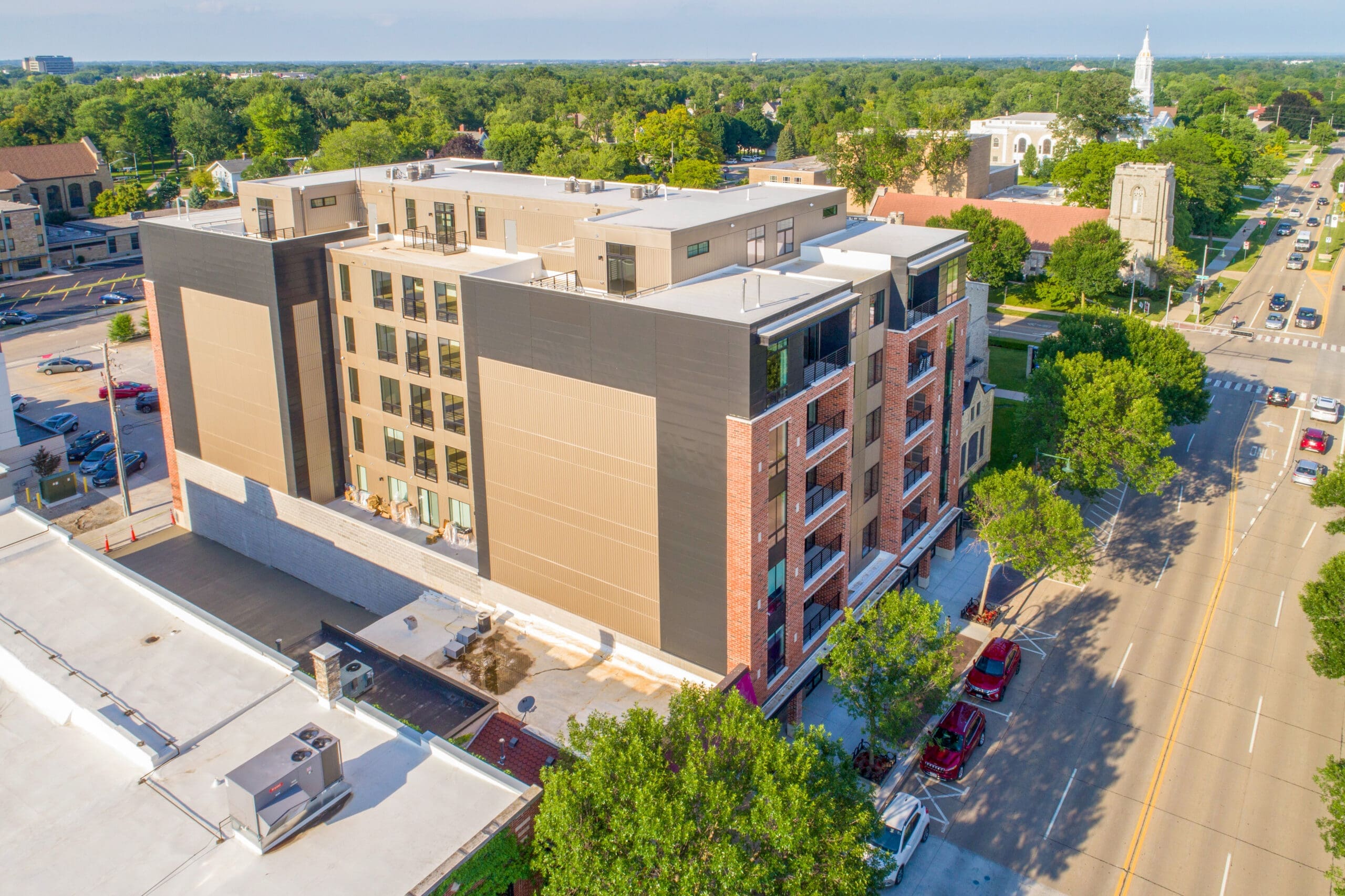 Aerial shot of modern mid-rise residential apartment, prime location next to tree-lined street, ideal for real estate listings.