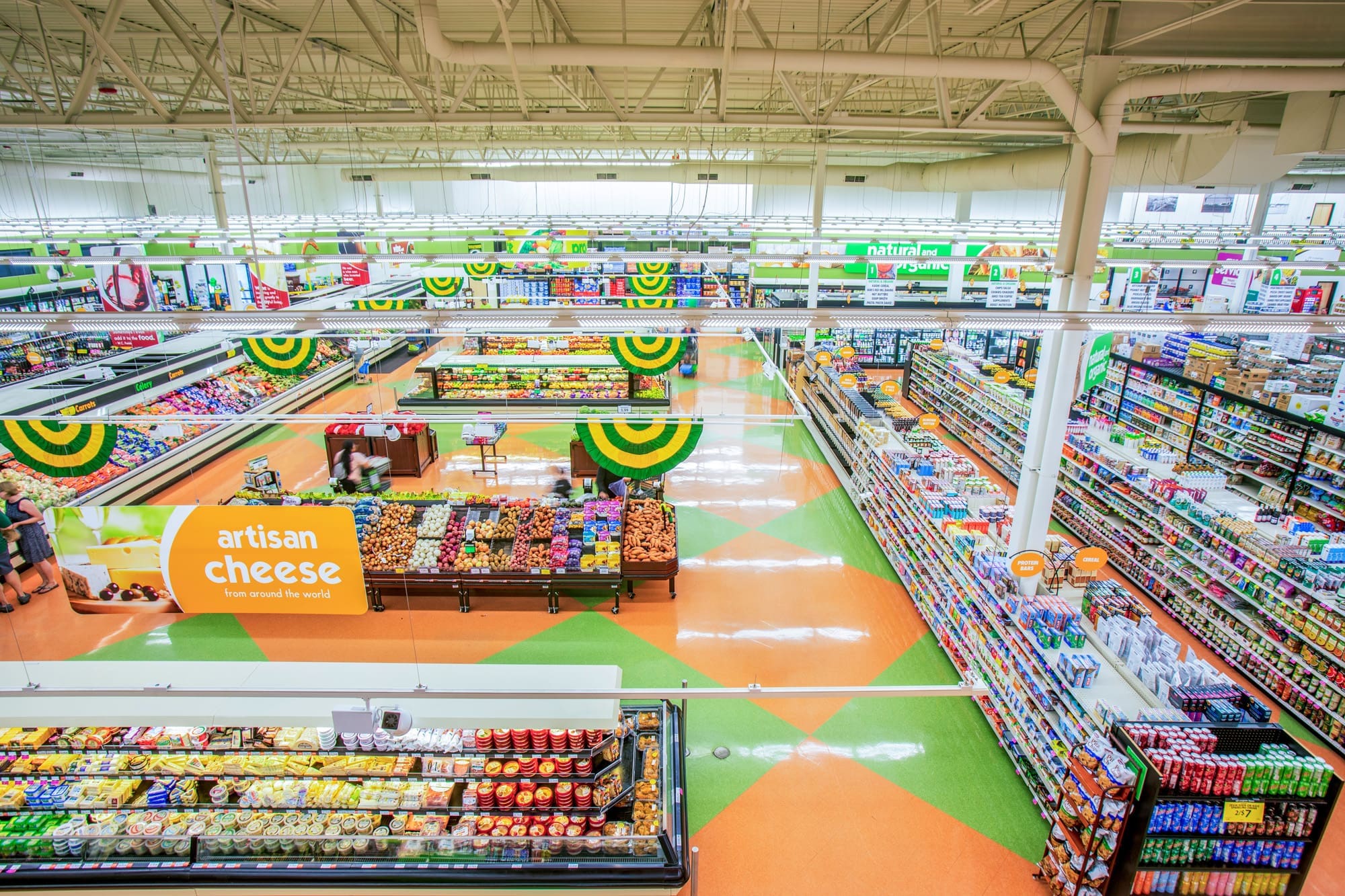 Commercial real estate photo of a well-lit supermarket showcasing organized aisles, fresh produce, and an artisan cheese section.