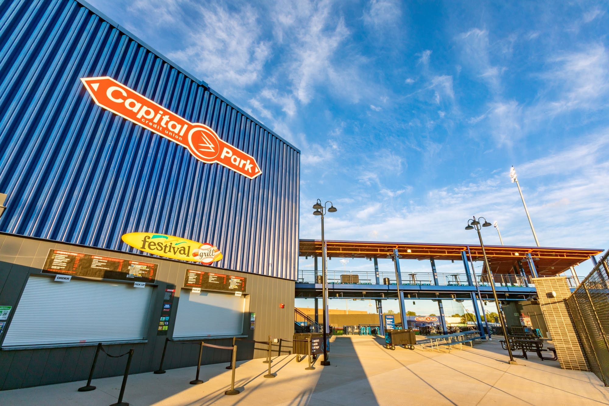Commercial property exterior at Capital Park stadium featuring a blue building, grill stand, and covered seating under clear skies.