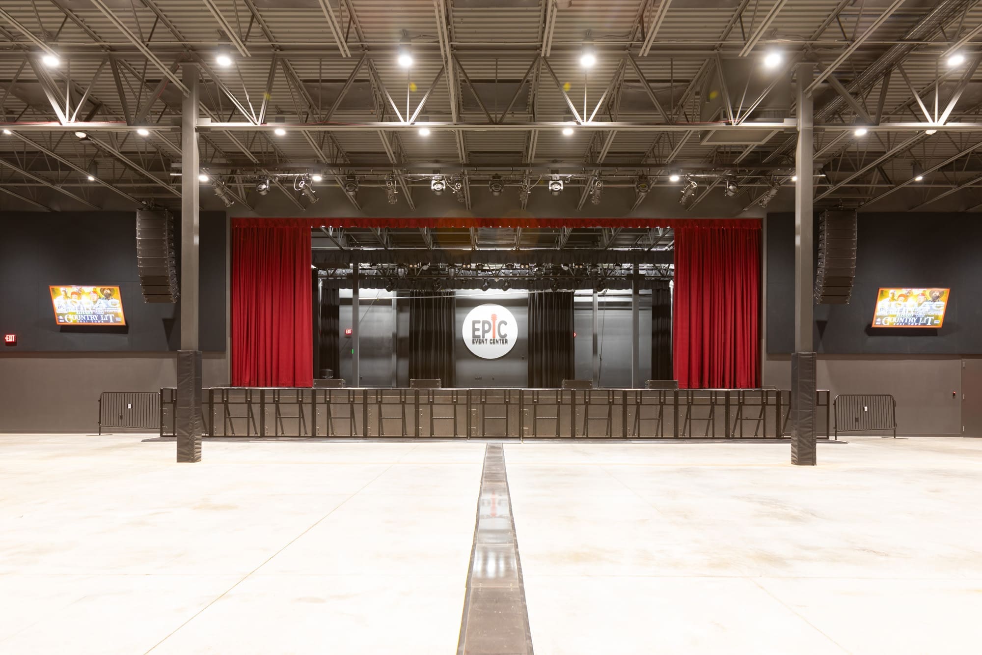 Spacious commercial event space with stage, red curtains, AV setup, dual side screens, and EPIC Event Center branding—ideal venue listing.
