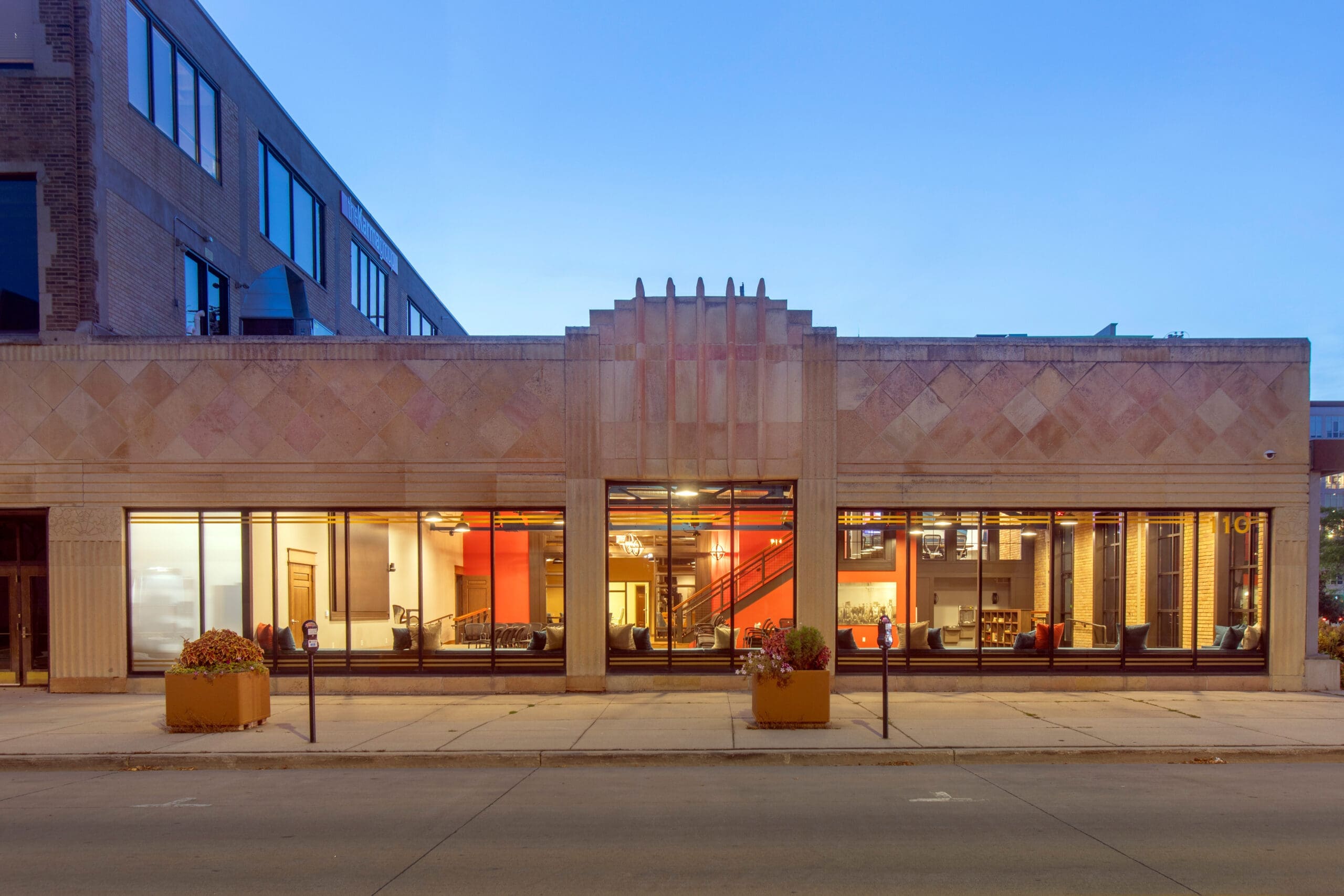 Commercial real estate listing: One-story Art Deco building, large glass windows, potted plants, modern interior with red staircase.