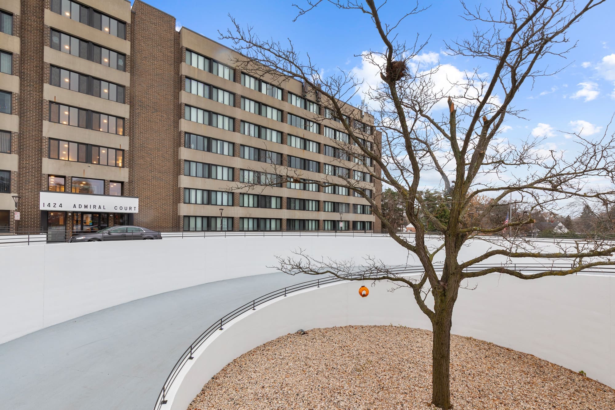 Curved driveway with landscaped gravel bed and mature tree in front of multi-story residential apartment at 1424 Admiral Court.