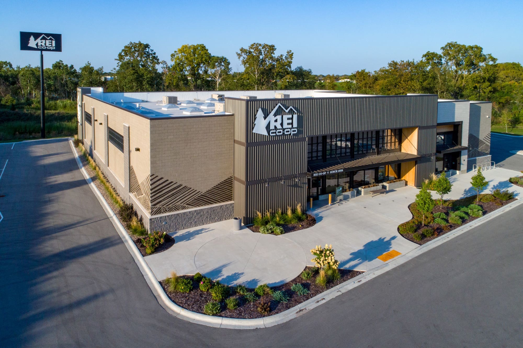 Commercial property photo of a modern REI Co-op with spacious parking, lush landscaping, and prominent signage, ideal retail location.