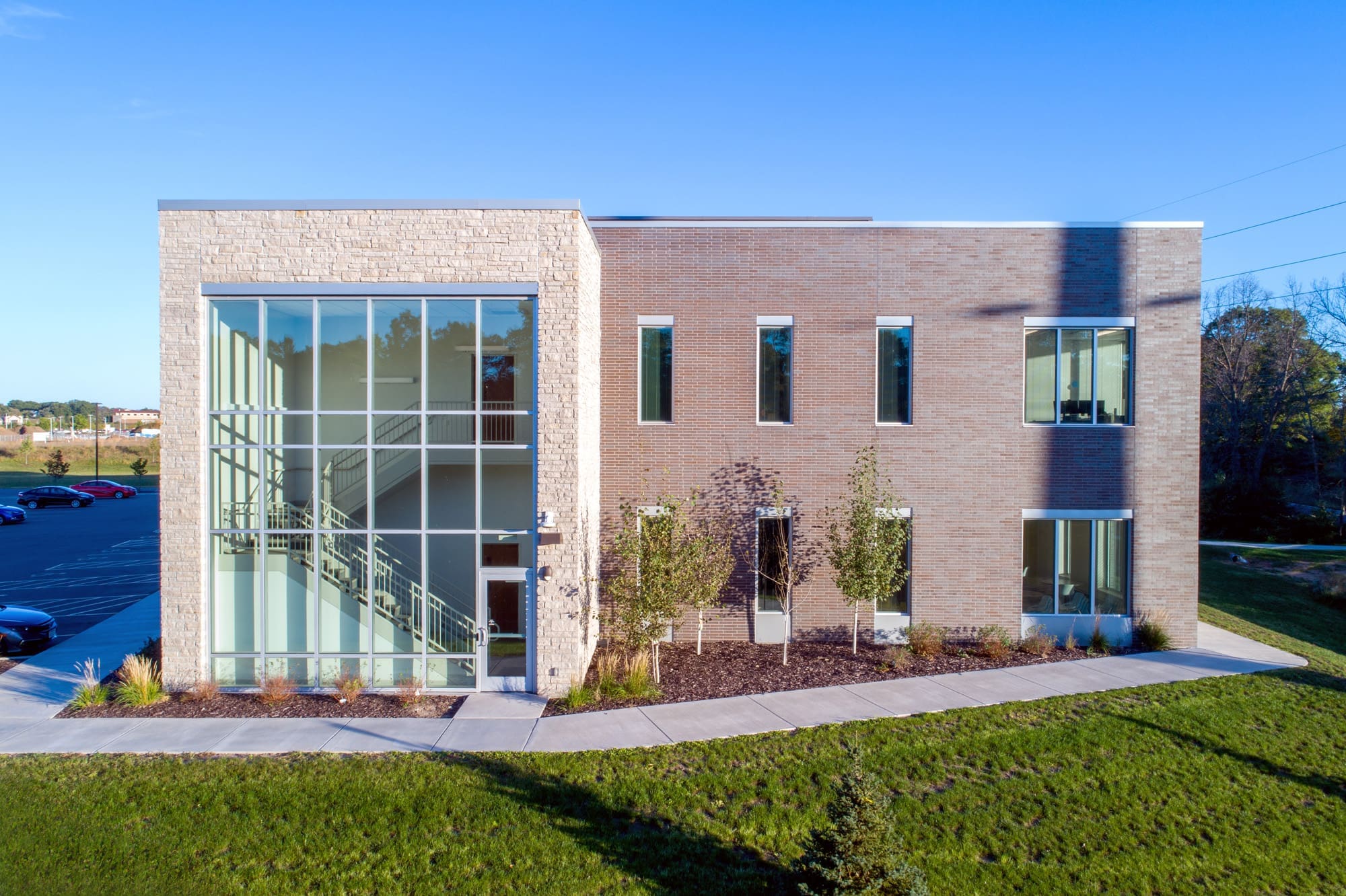 Contemporary two-story commercial property with brick and glass exterior, expansive windows, landscaped grounds, and blue sky.