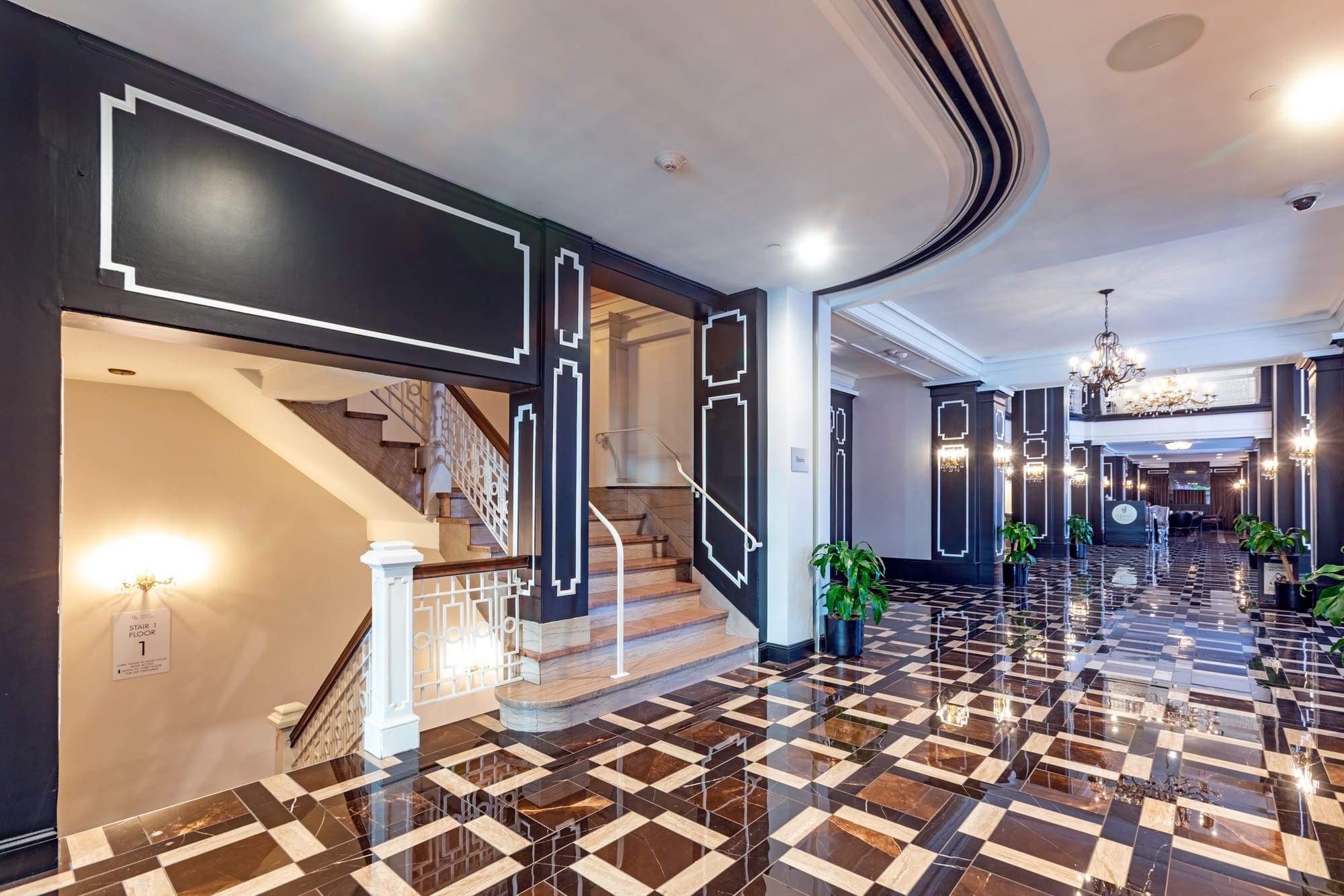 Modern commercial property lobby featuring a polished geometric floor, black and white walls, chandeliers, plants, and staircase.