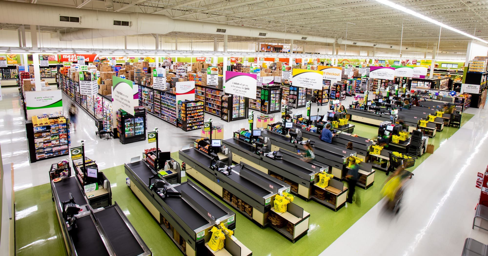 Commercial real estate photo of a spacious, well-lit supermarket interior with multiple checkout lanes, carts, and stocked grocery aisles.