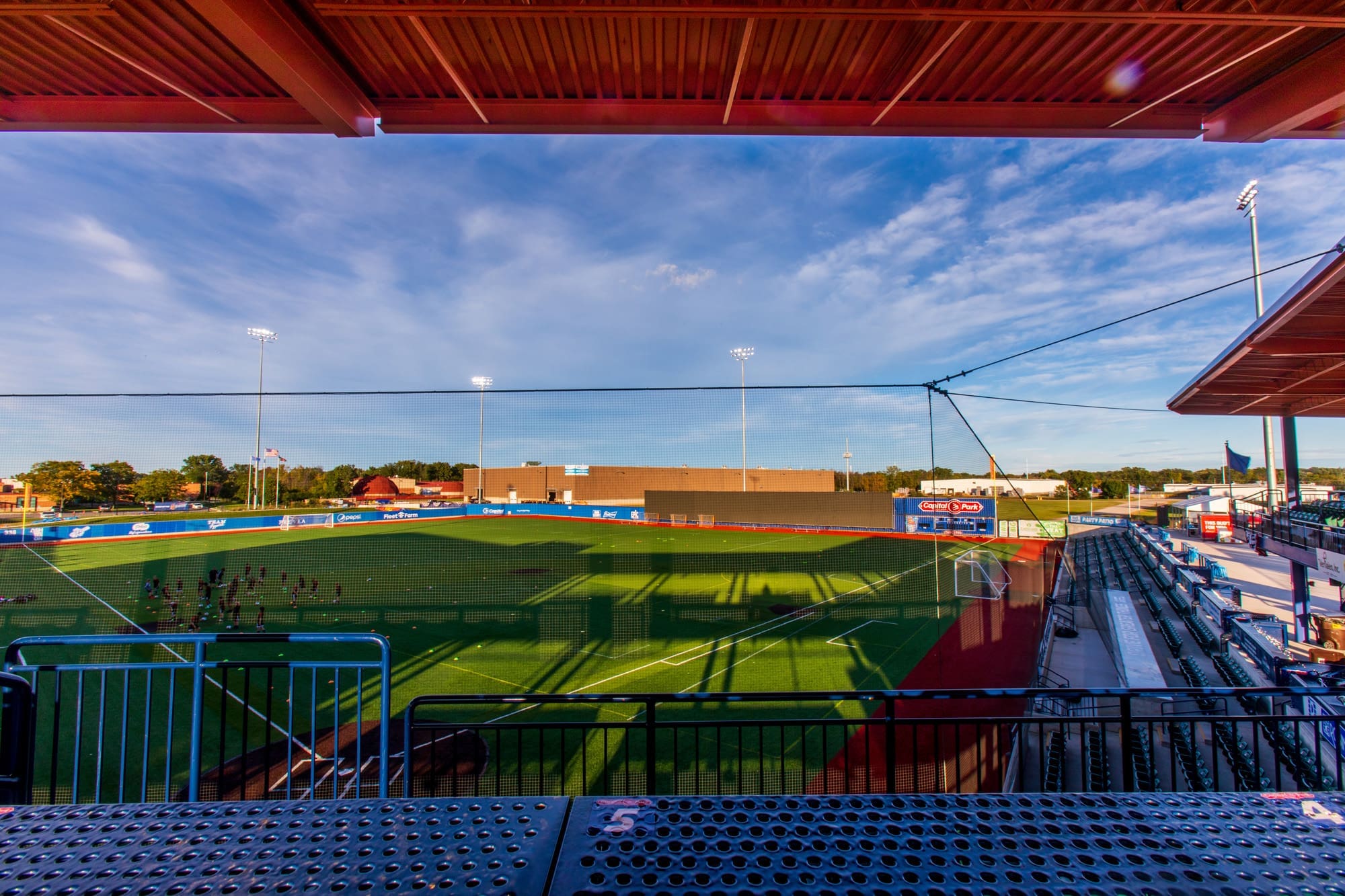 Commercial property photo of an empty outdoor stadium with artificial turf, covered seating, and scoreboard, ideal for real estate listings.