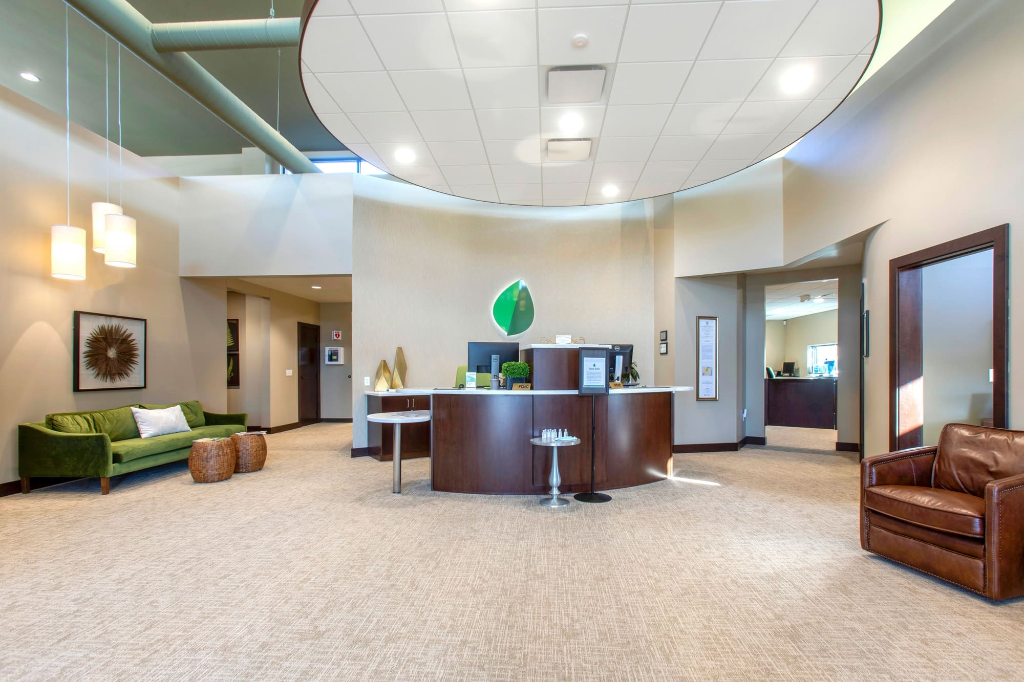 Commercial property lobby featuring a circular reception desk, stylish furniture, beige carpet, and bright lighting for real estate showcase.