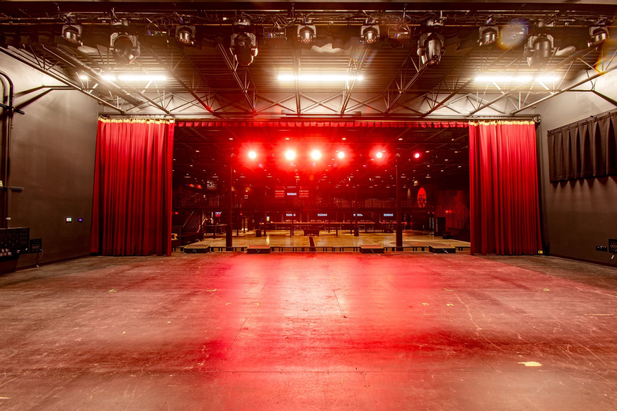 Commercial real estate photo showing empty concert hall interior from stage, featuring red curtains, overhead lights, and seating rows.