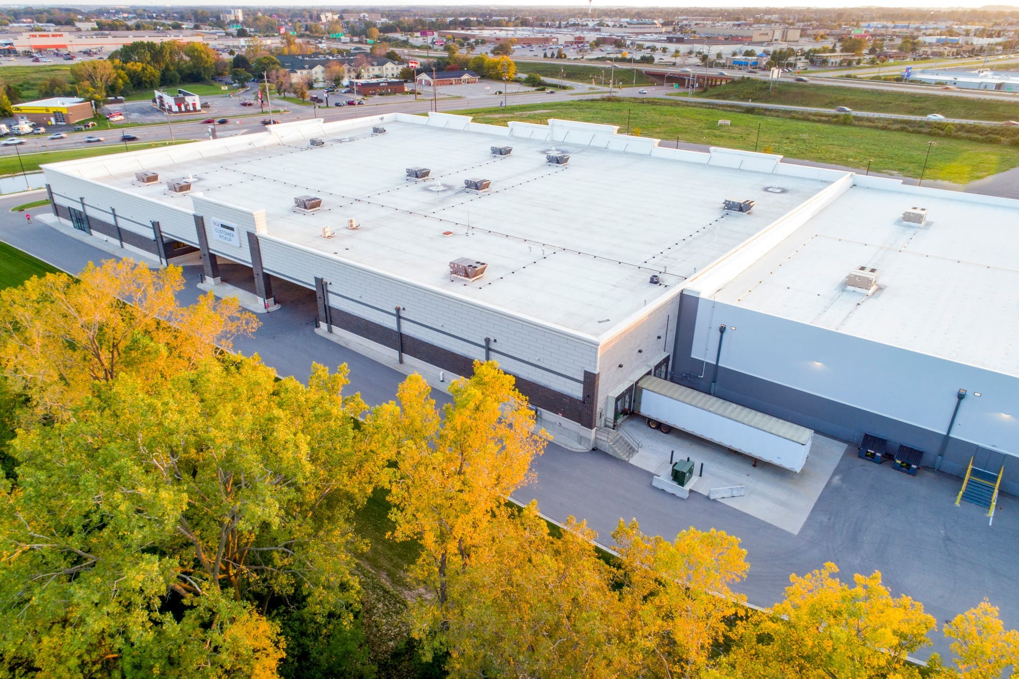 Commercial warehouse property with white roof, surrounded by autumn trees near roadway, ideal for industrial real estate listing.