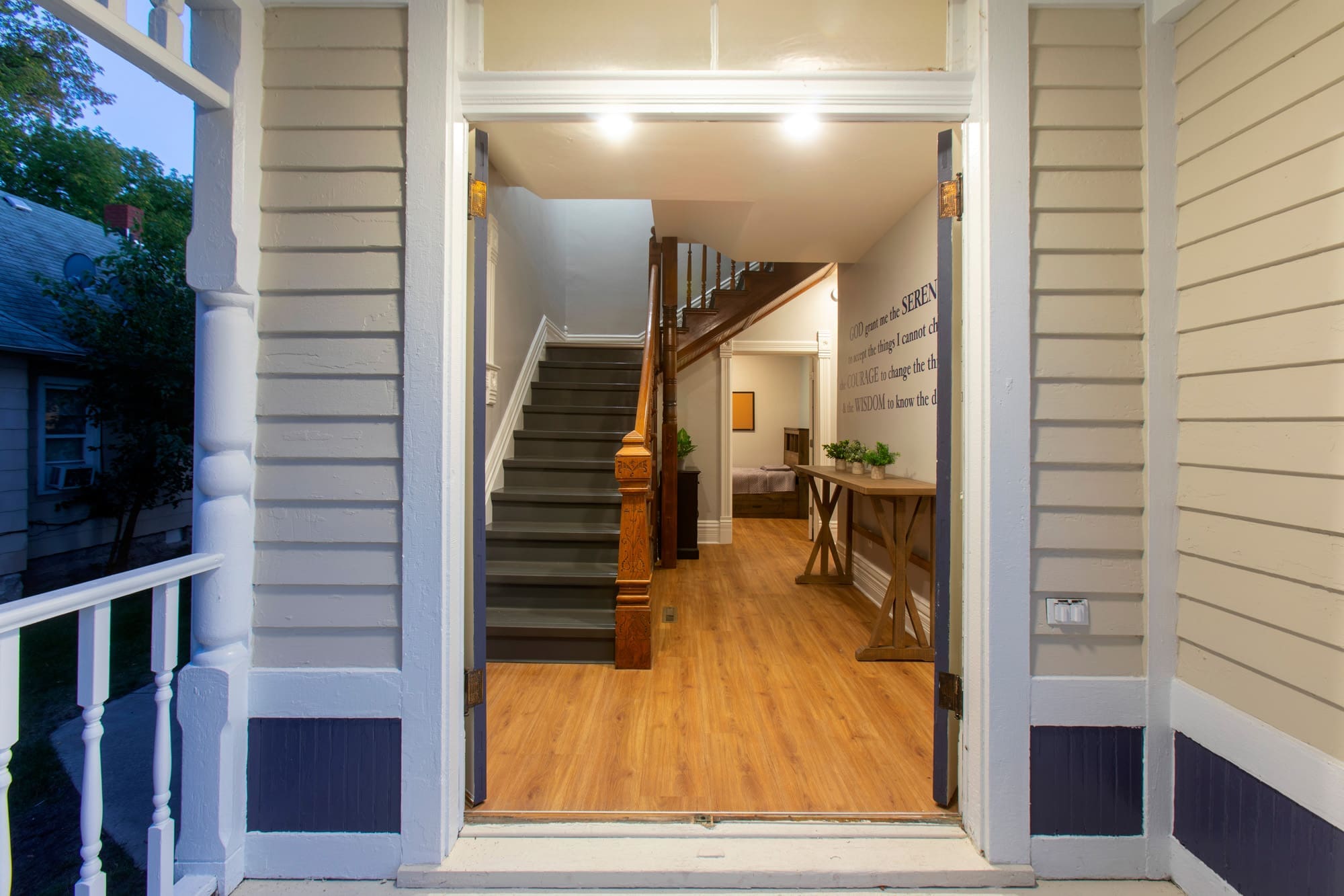 Residential real estate entryway photo with wood flooring, staircase with wood railing, and hallway table along the right wall.