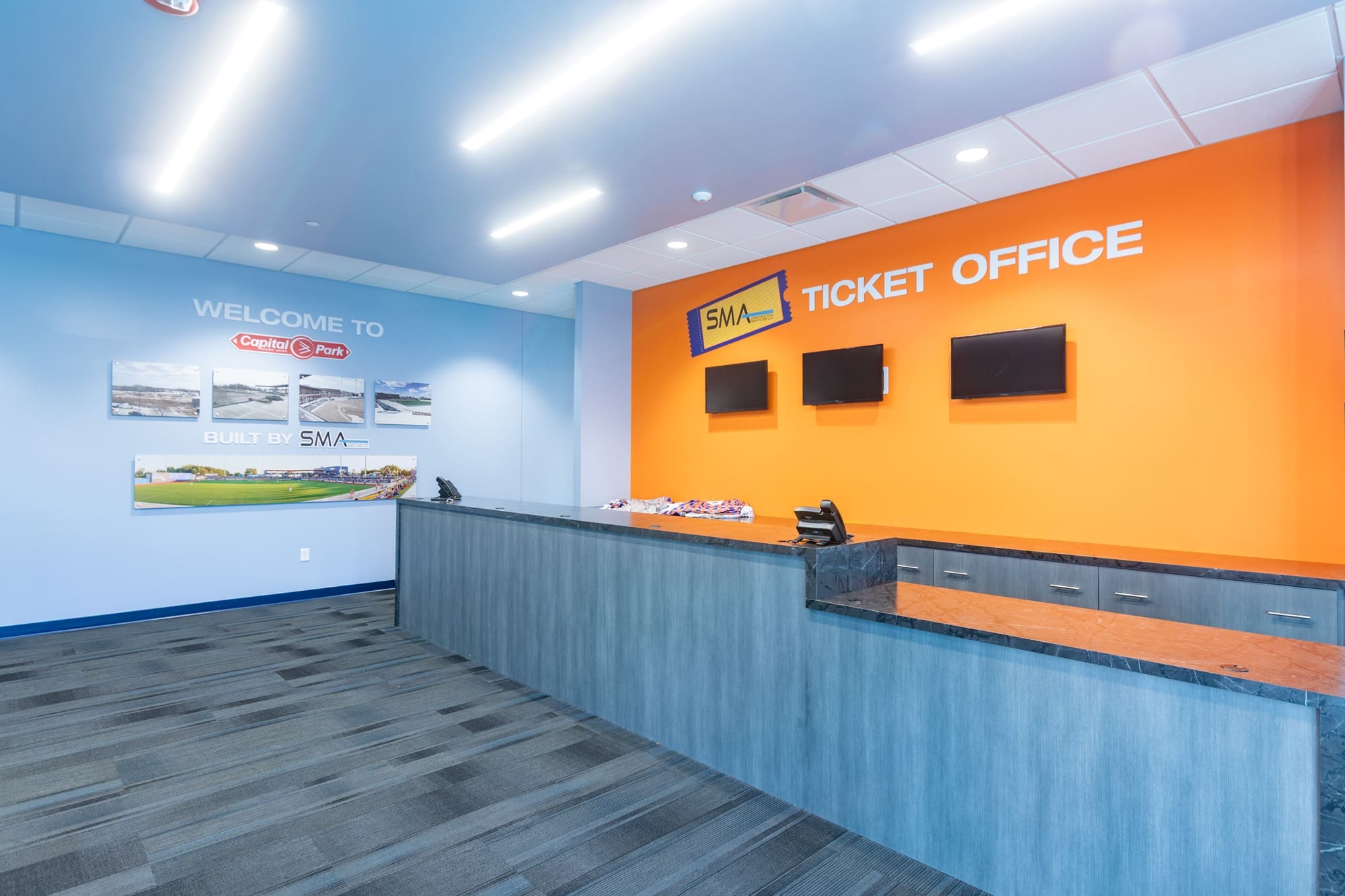 Commercial property interior featuring a modern ticket office, blue and orange decor, computer terminals, and wall displays behind the desk.