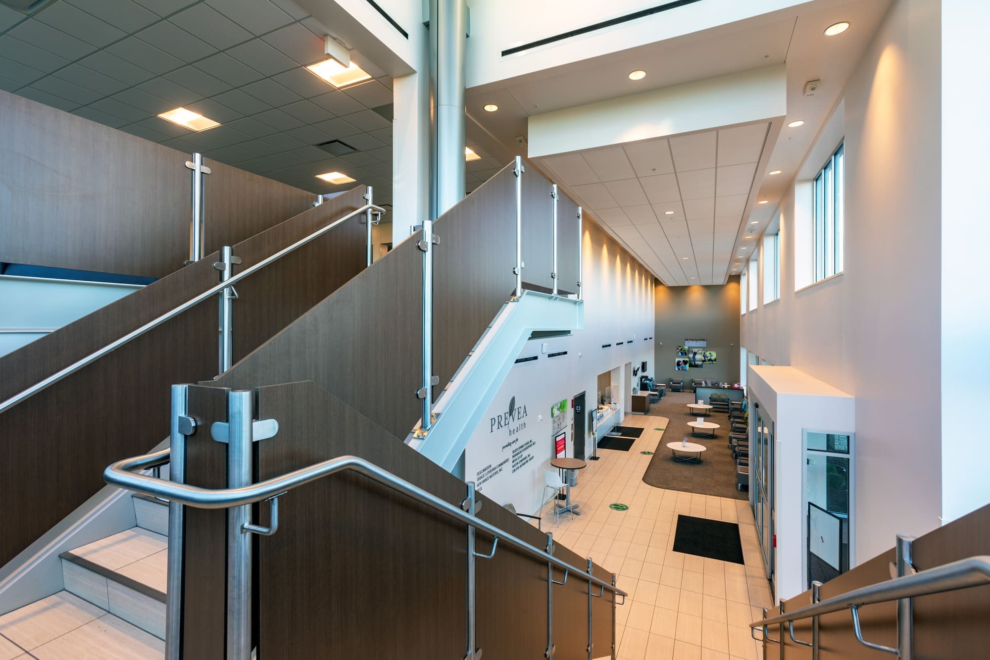 Spacious commercial property interior with wide stairs, metal railings, wood accents, seating areas, and large windows for natural light.