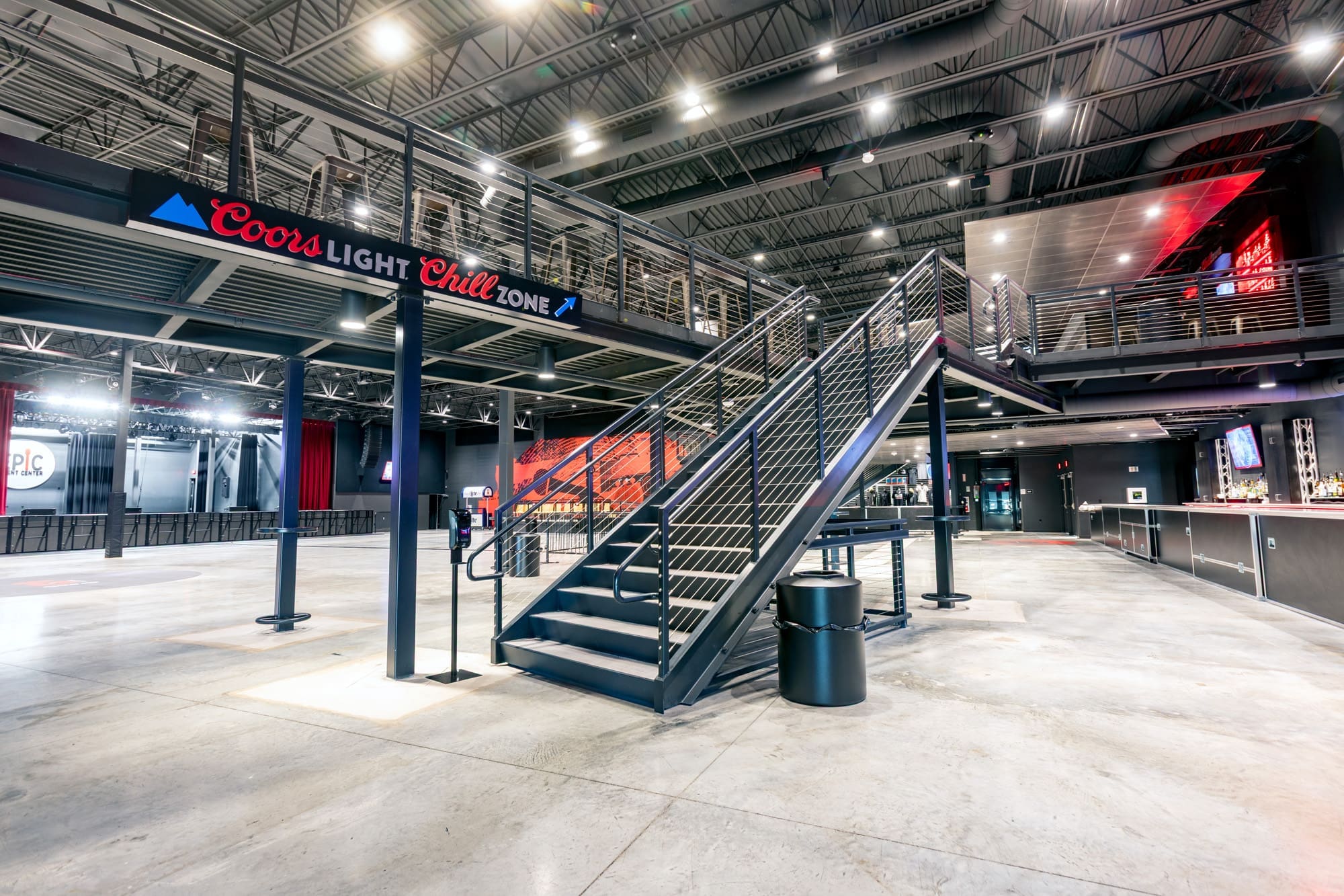 Expansive commercial property interior featuring concrete floors, upper-level lounge, and bar area; ideal for events or business use.