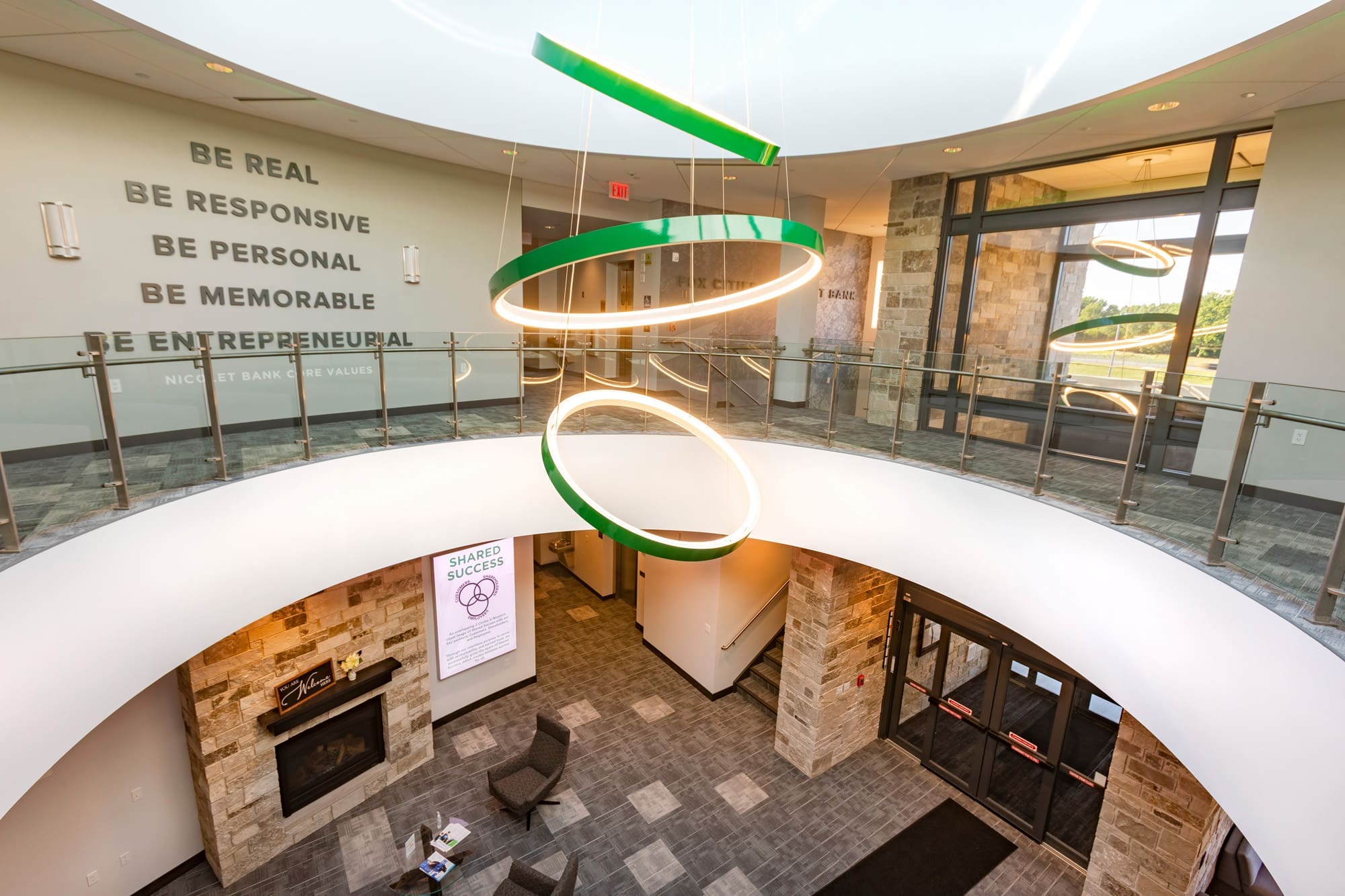 Spacious commercial office atrium featuring modern lighting, stone walls, glass railings, lounge seating, and motivational wall text.
