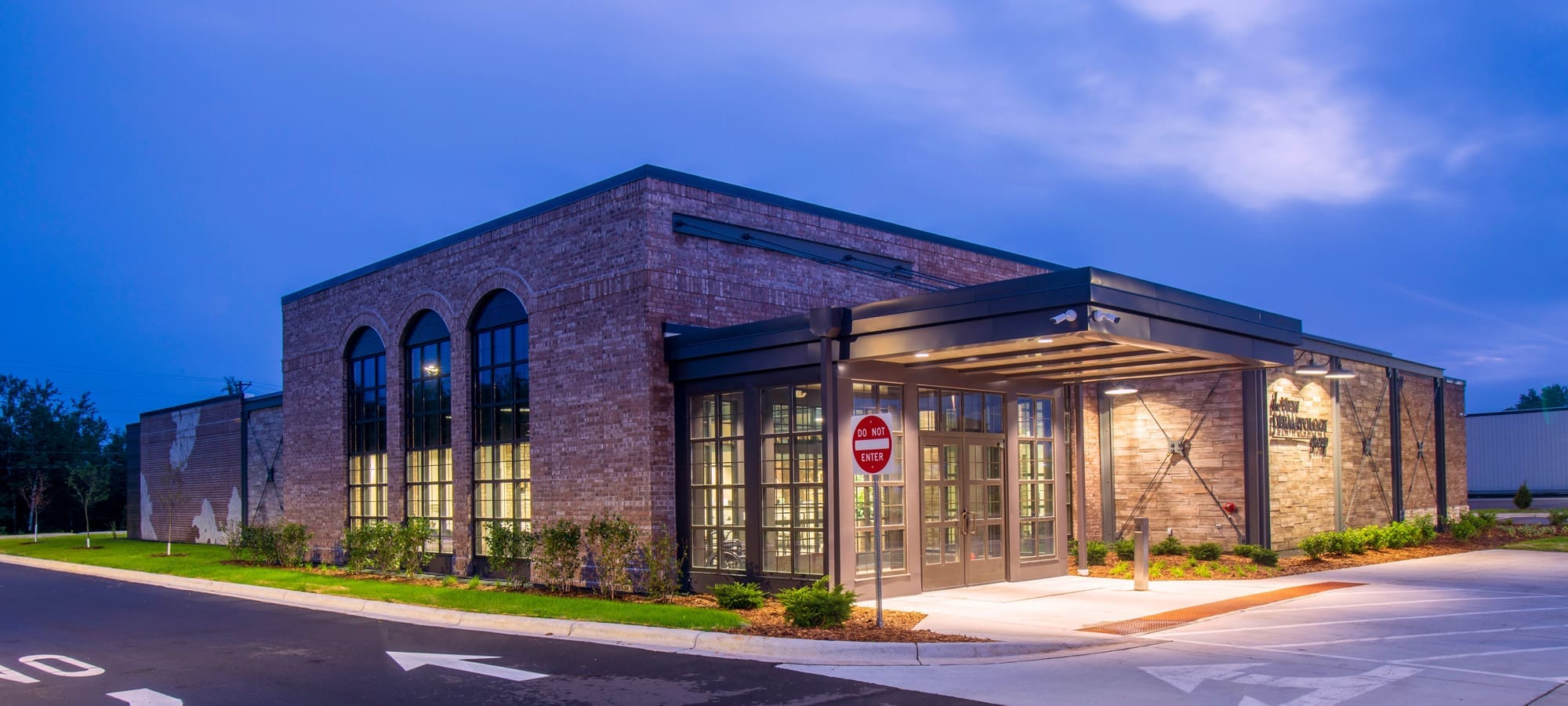 Commercial property exterior at dusk, featuring modern brickwork, arched windows, covered entry, and illuminated architecture.
