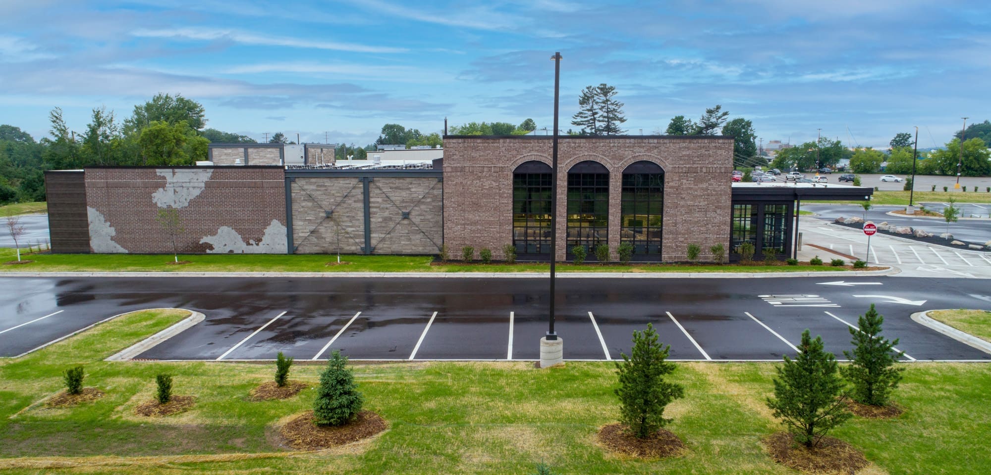 Commercial property for sale: brick building with large windows, empty parking lot, landscaping, overcast sky—real estate photo.