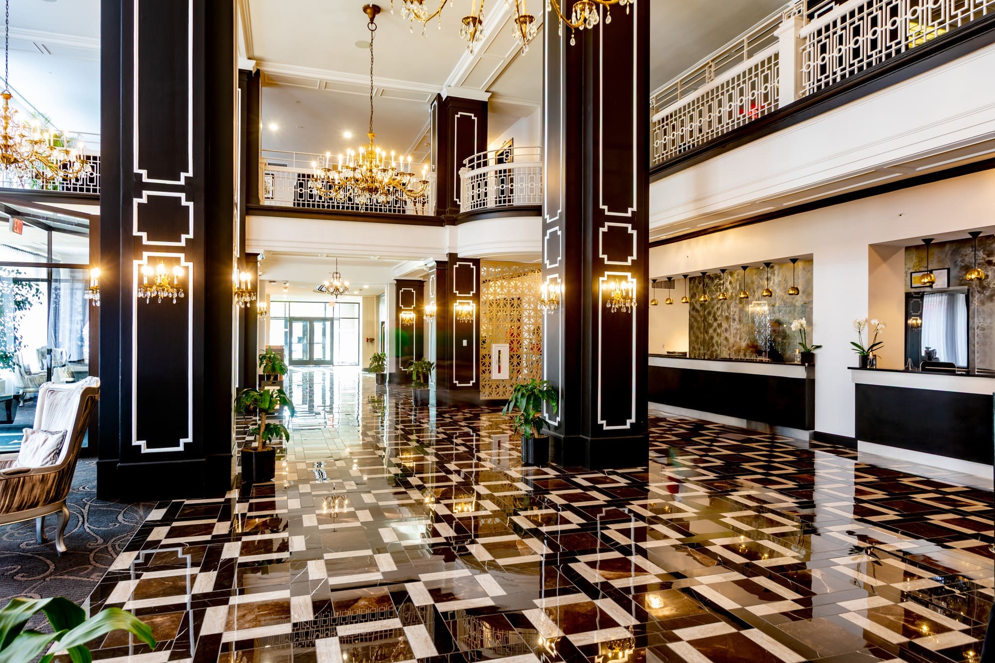 Luxury commercial property lobby featuring glossy patterned flooring, black and white columns, chandeliers, seating area, and front desk.