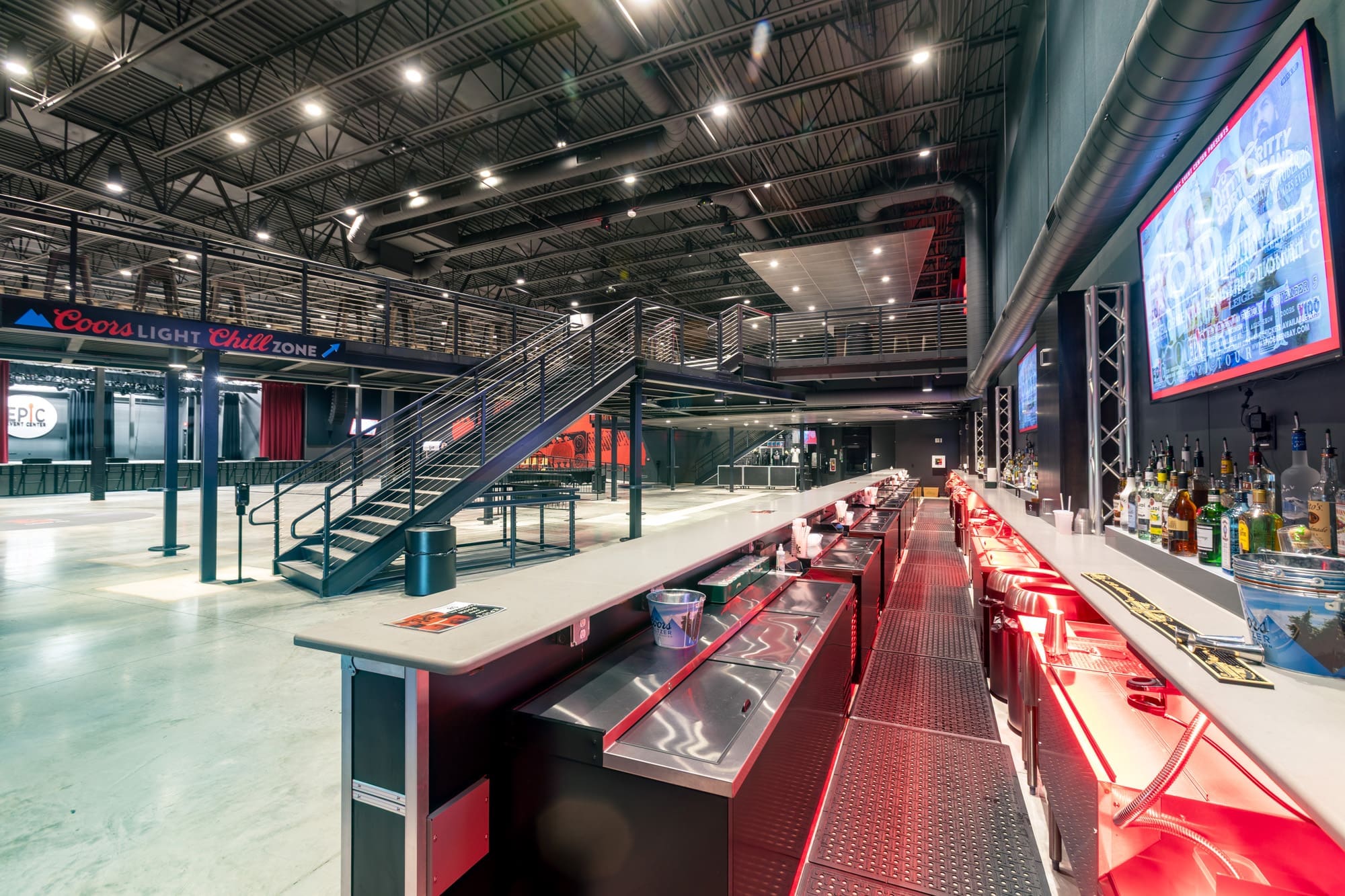 Commercial property featuring a modern bar, event space, mezzanine level, metal stairs, red accent lighting, and open floor plan.