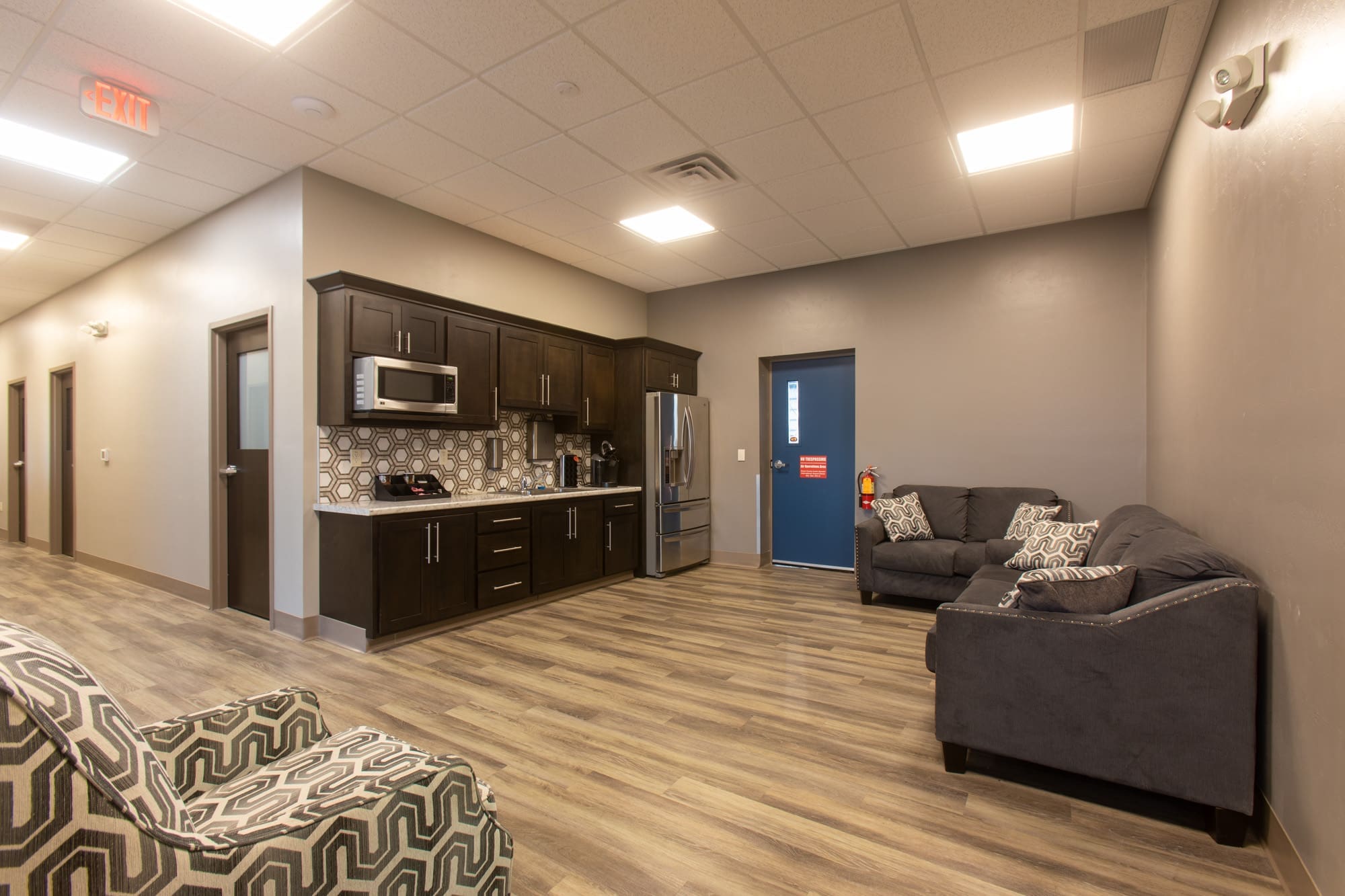 Residential lounge area with kitchenette, stainless steel appliances, wood-style floors, and stylish furnishings for real estate photos.