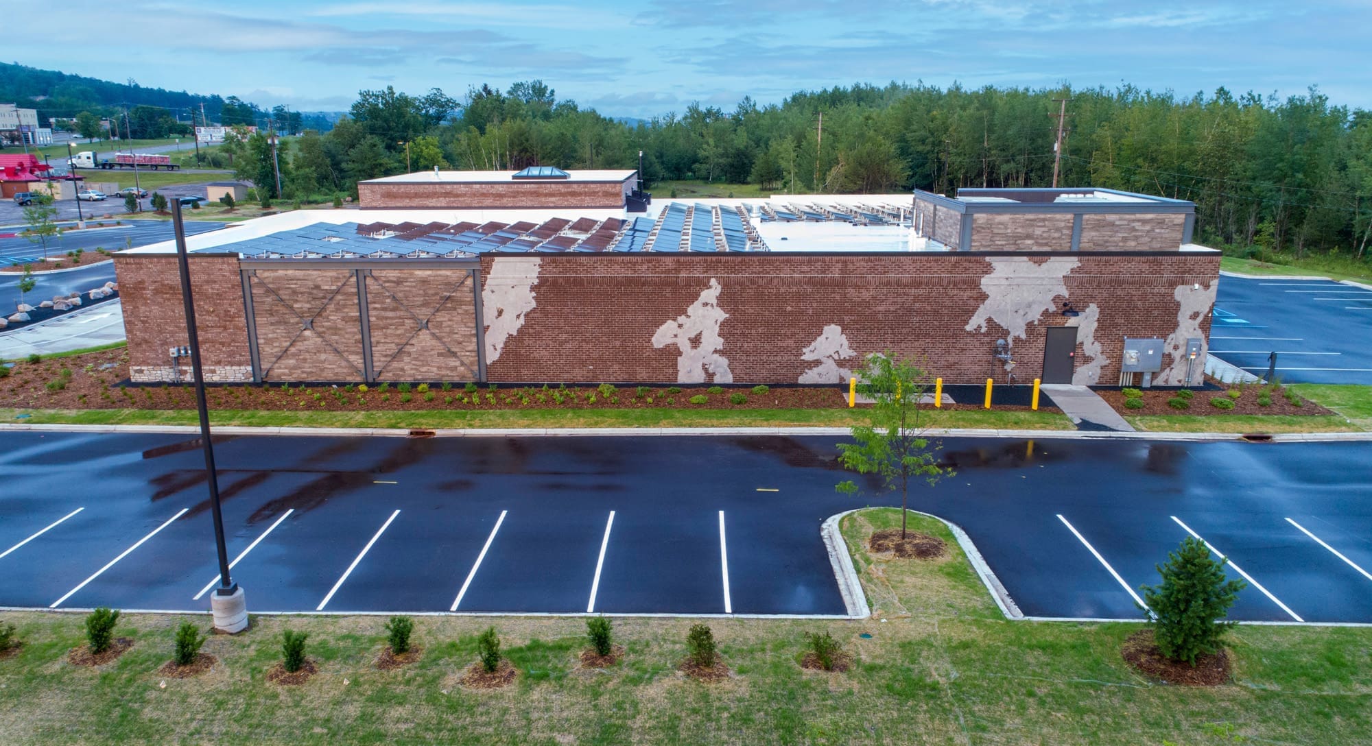 Commercial property featuring a spacious brick building and empty parking lot, set among trees under a cloudy sky, ideal for leasing.