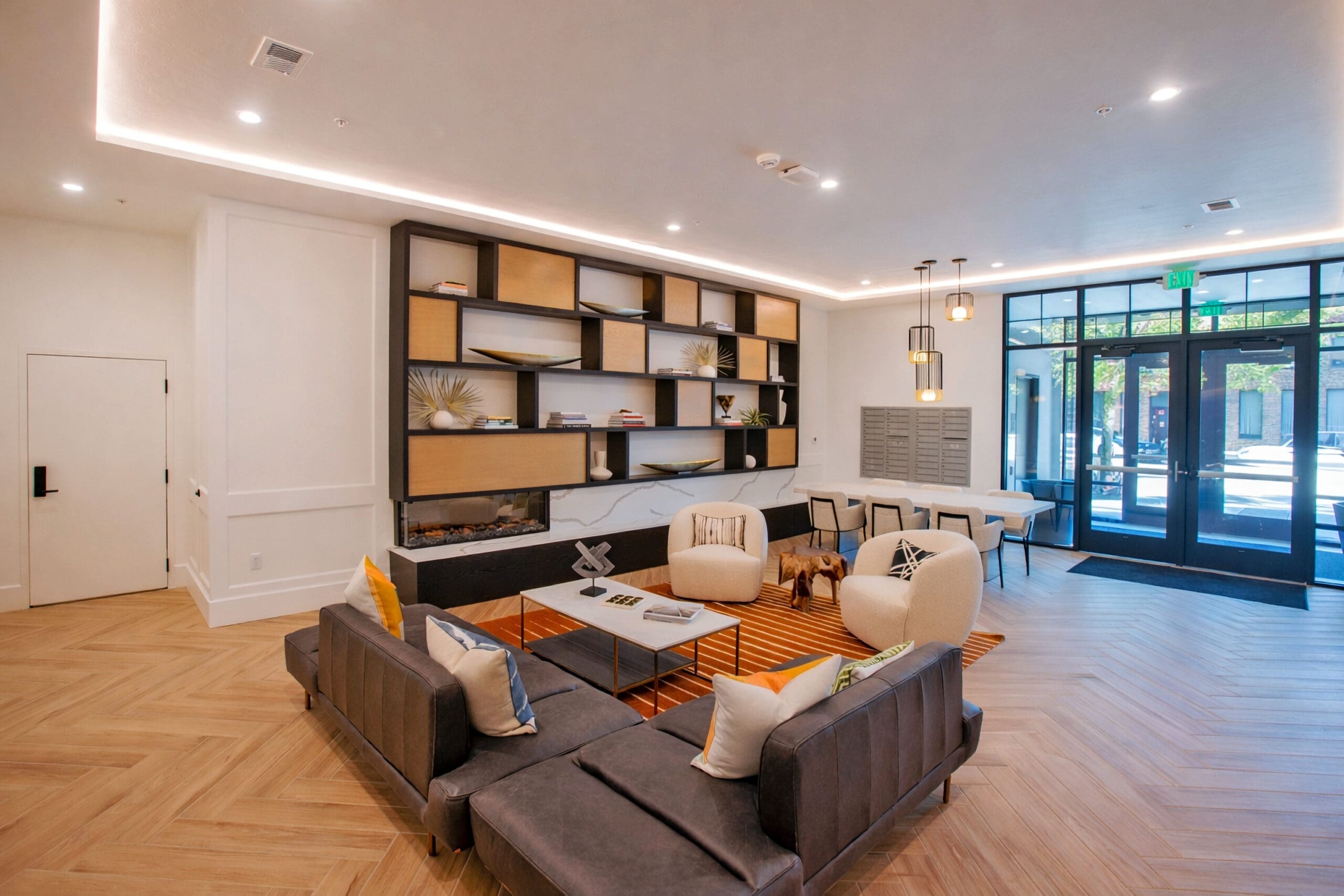 Spacious modern residential lounge with gray sofas, beige armchairs, coffee table, open shelving, and large windows with natural light.