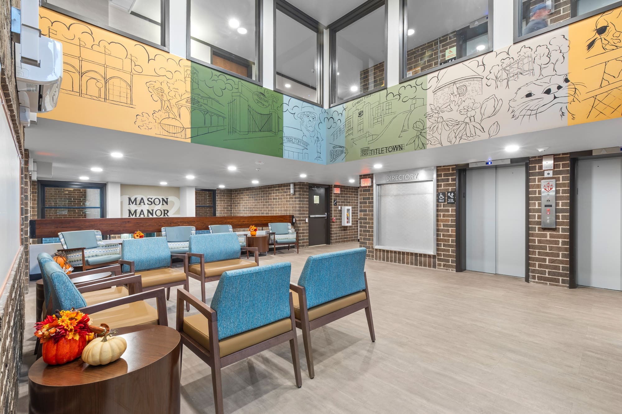 Spacious Mason Manor lobby with blue seating, autumn decor, brick walls, elevators, and mural—ideal for commercial real estate.