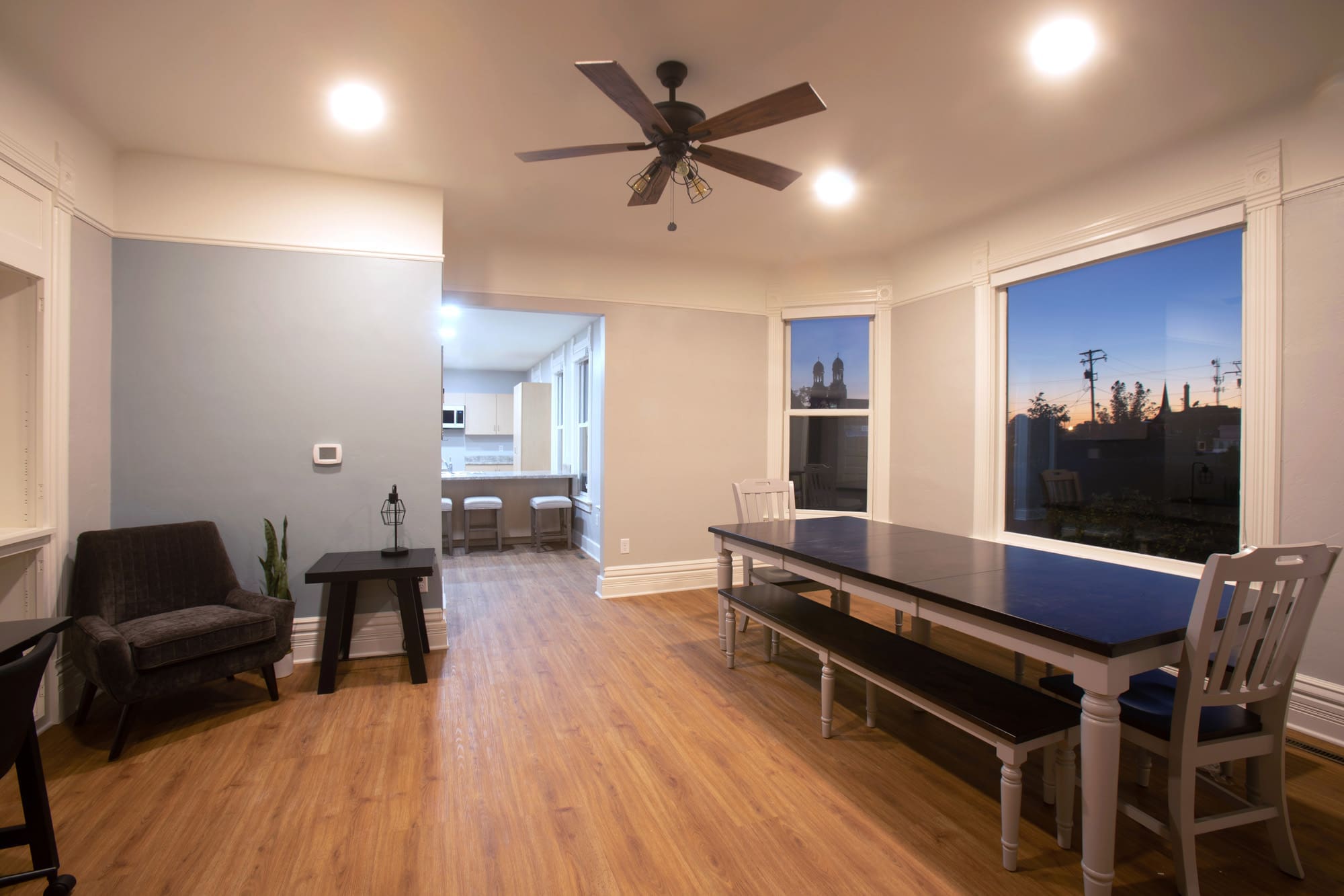Residential dining room with large windows, wood floors, ceiling fan, and open concept kitchen—ideal for real estate listings.