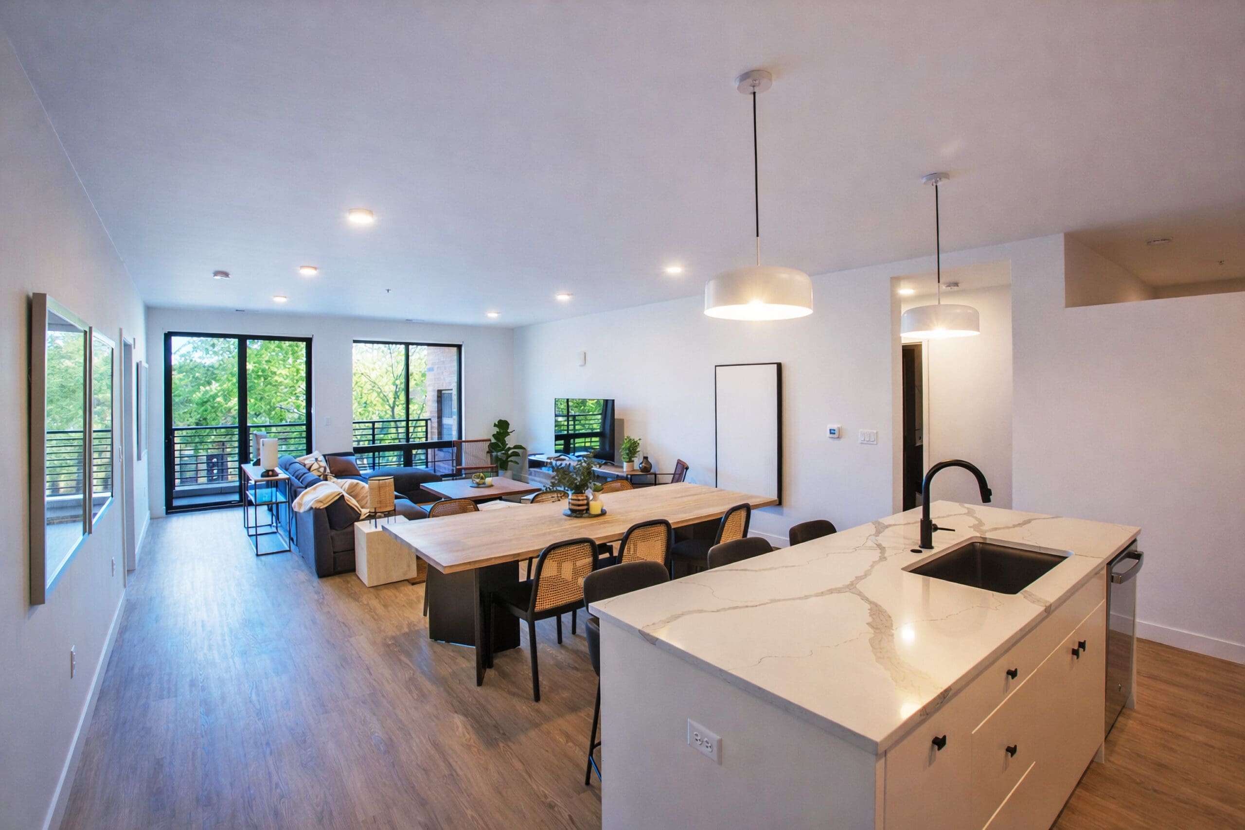 Spacious residential apartment with open-concept layout, kitchen island, dining area, large windows, and balcony with greenery view.