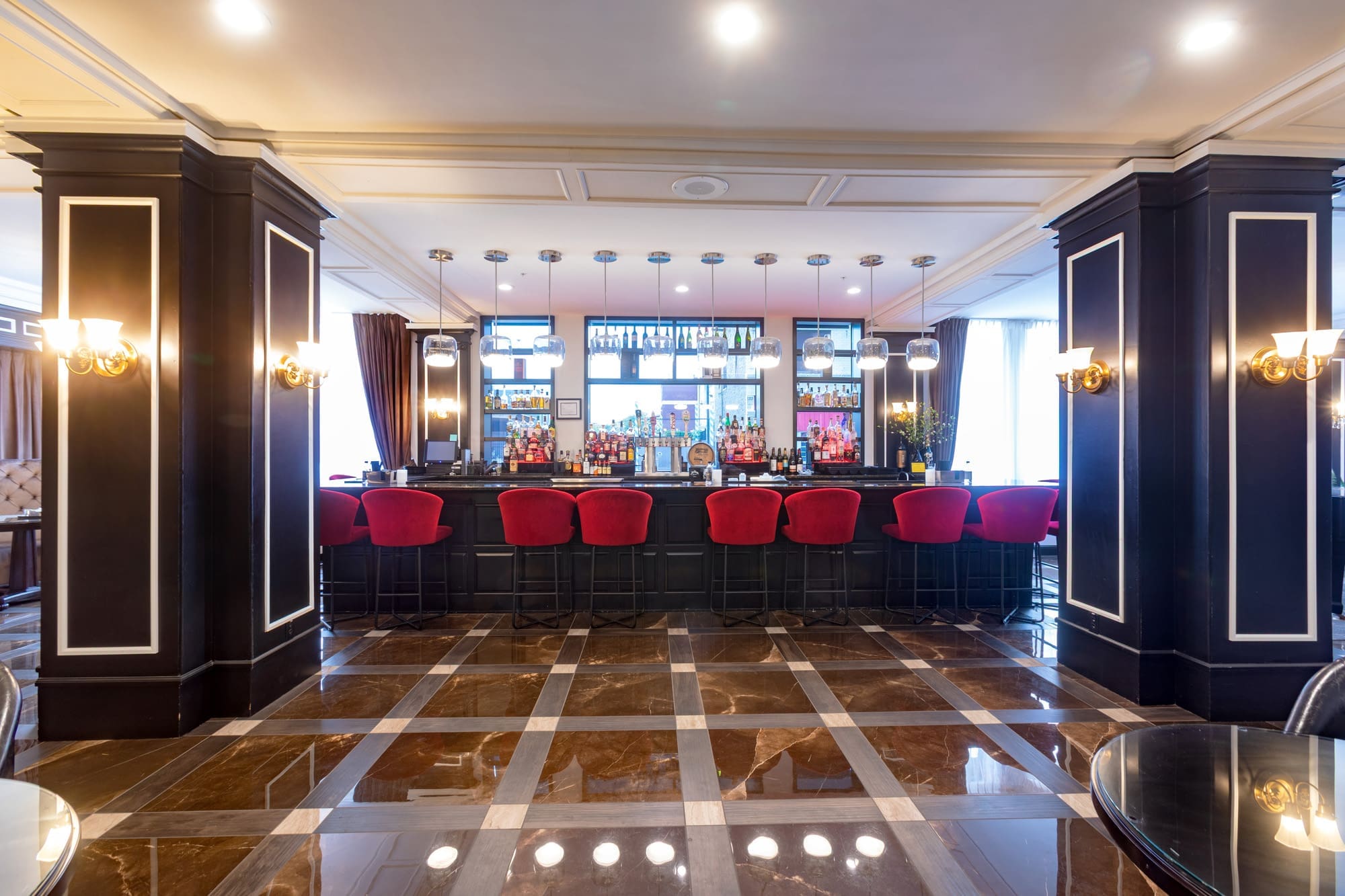 Commercial property bar area featuring red barstools, dark wood accents, mirrored shelving, and polished brown and white tile flooring.