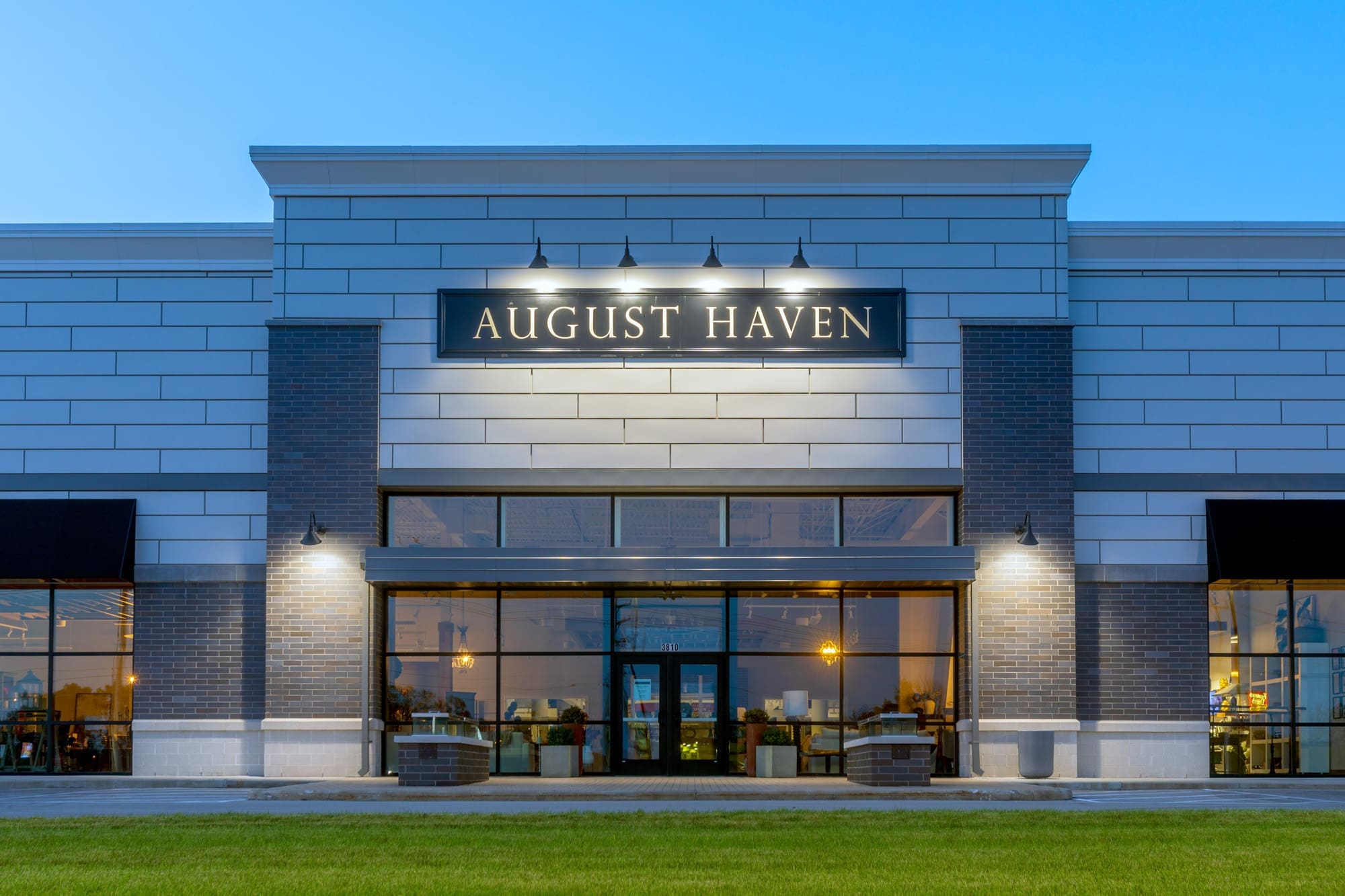 Commercial property exterior featuring August Haven furniture store, large windows, brick facade, and illuminated signage at dusk.