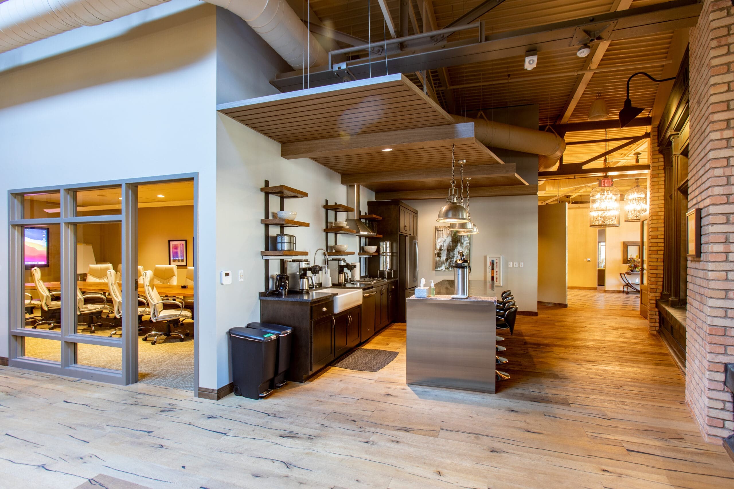 Commercial office kitchen with modern amenities, open shelving, bar counter, glass-walled conference room, wood flooring—ideal workspace.