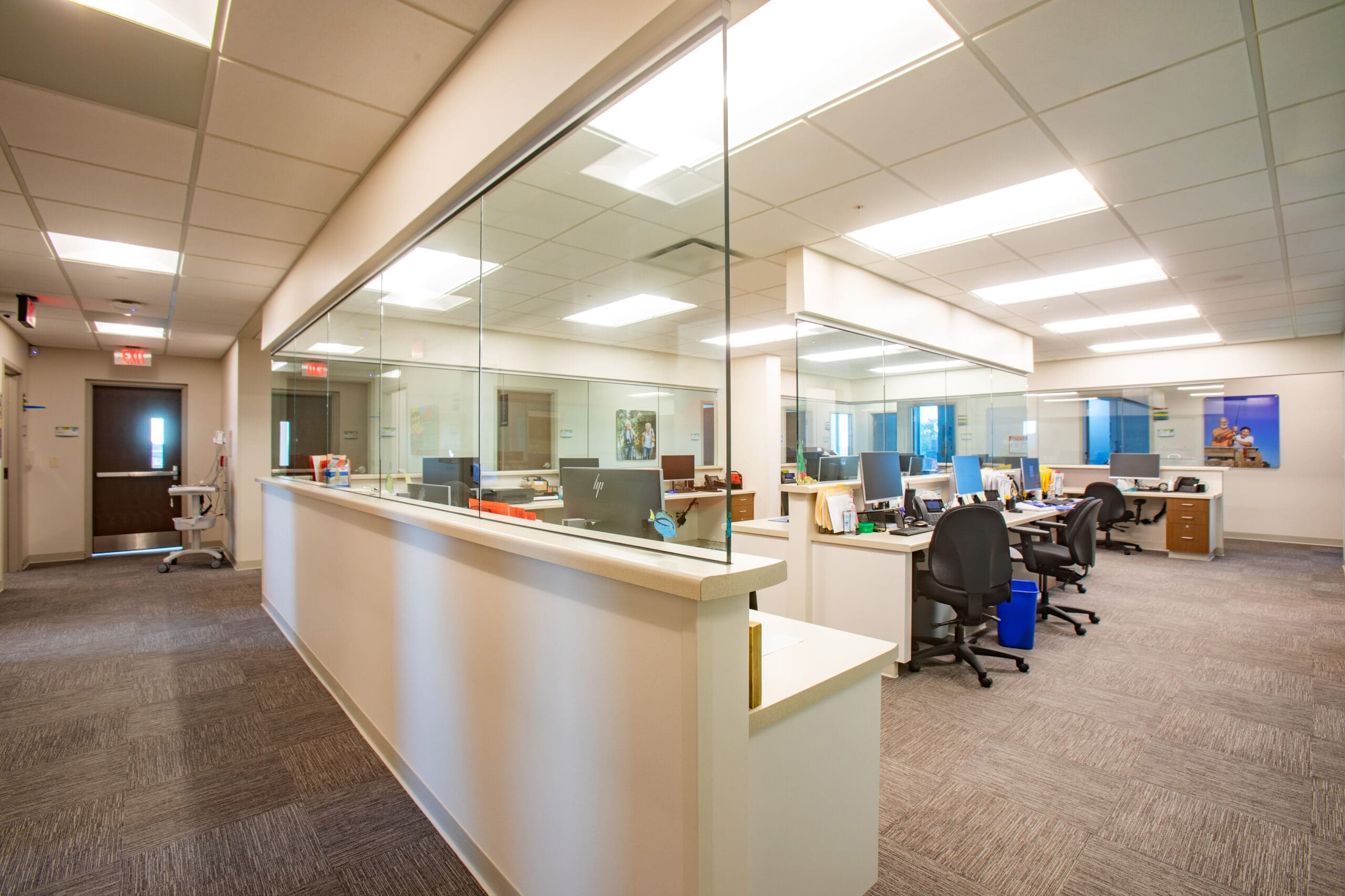 Commercial office for lease featuring open workspace, glass partitions, carpeted floors, ample lighting, and modern furnishings.