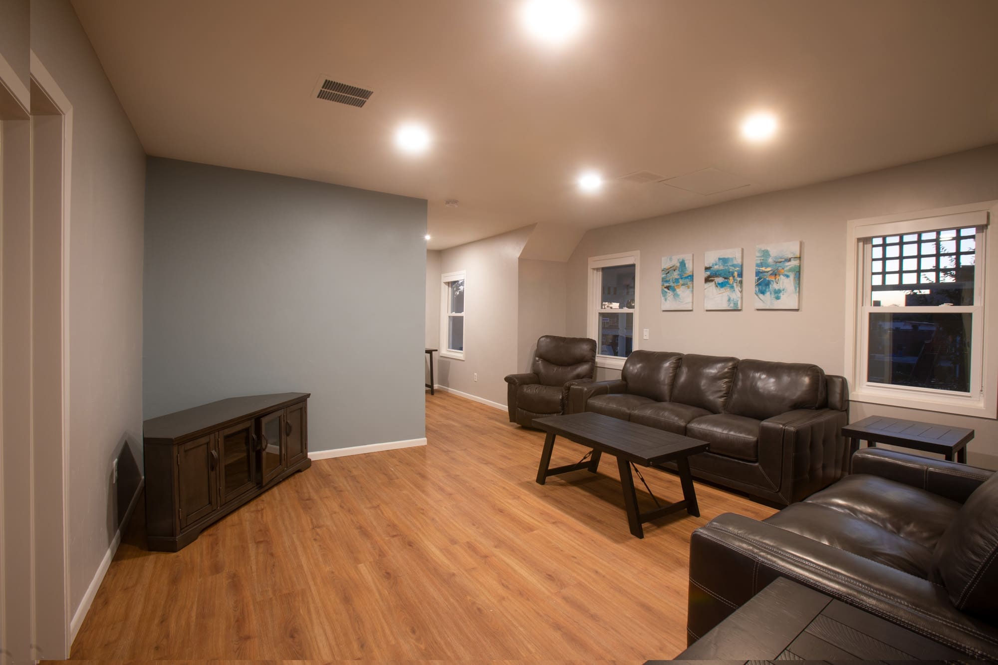Modern residential living room with brown leather sofas, wood coffee table, TV stand, wall art, and light wood floors. Realtor photo.