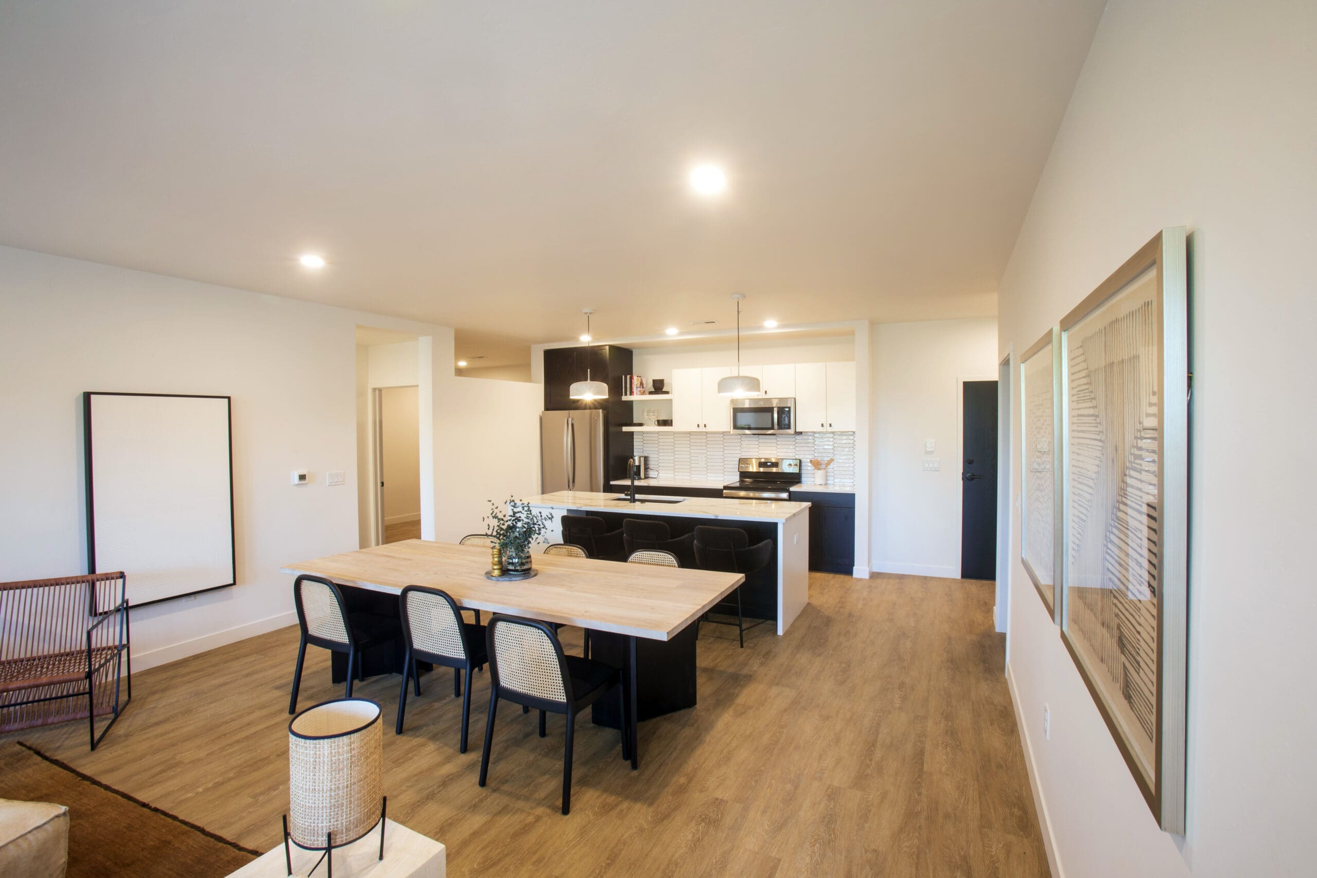 Contemporary open-concept kitchen and dining space in residential property, wood flooring, black-white cabinetry, table, six chairs.