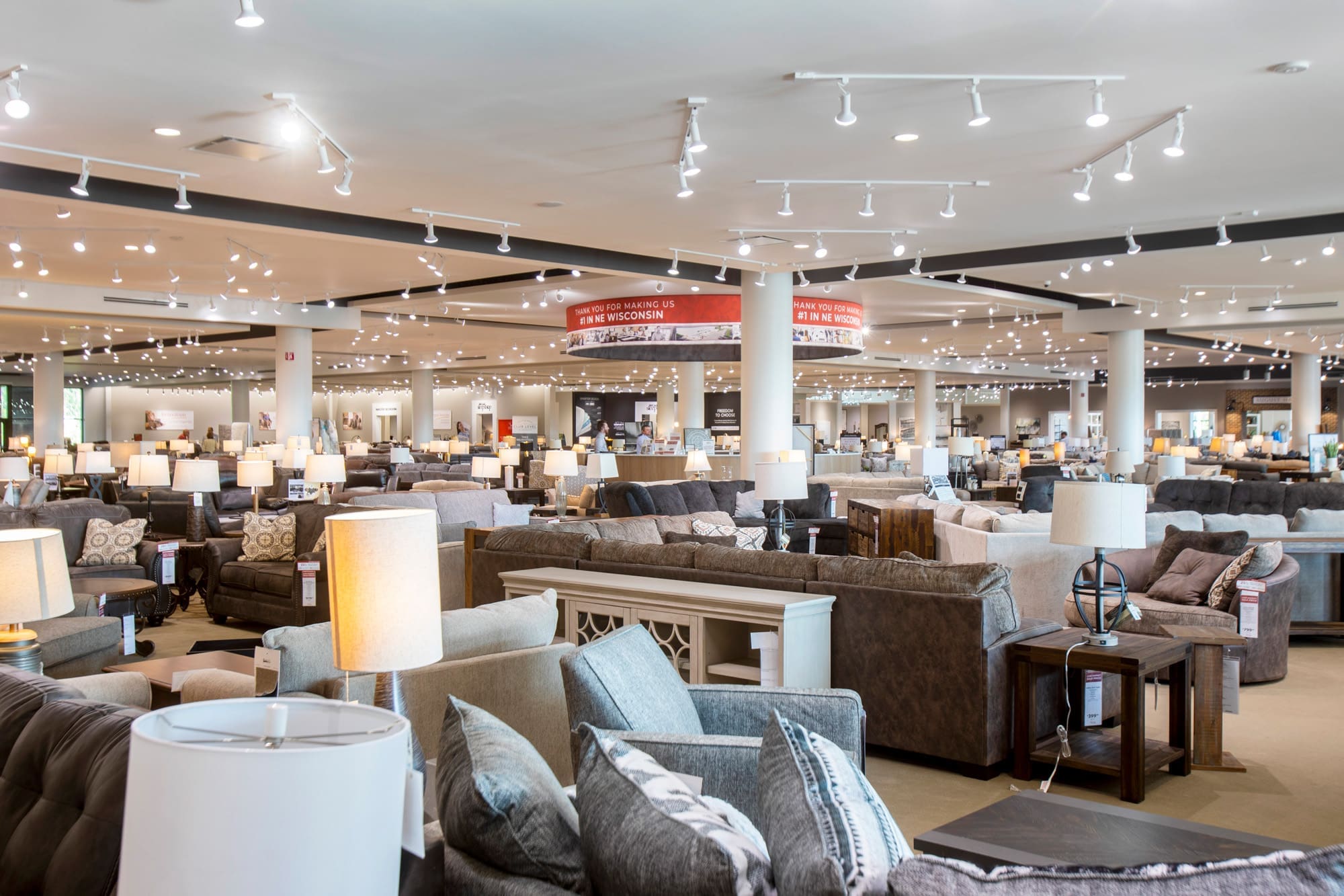 Spacious commercial showroom with stylish sofas, tables, and lighting, ideal for real estate listings; bright, inviting interior.