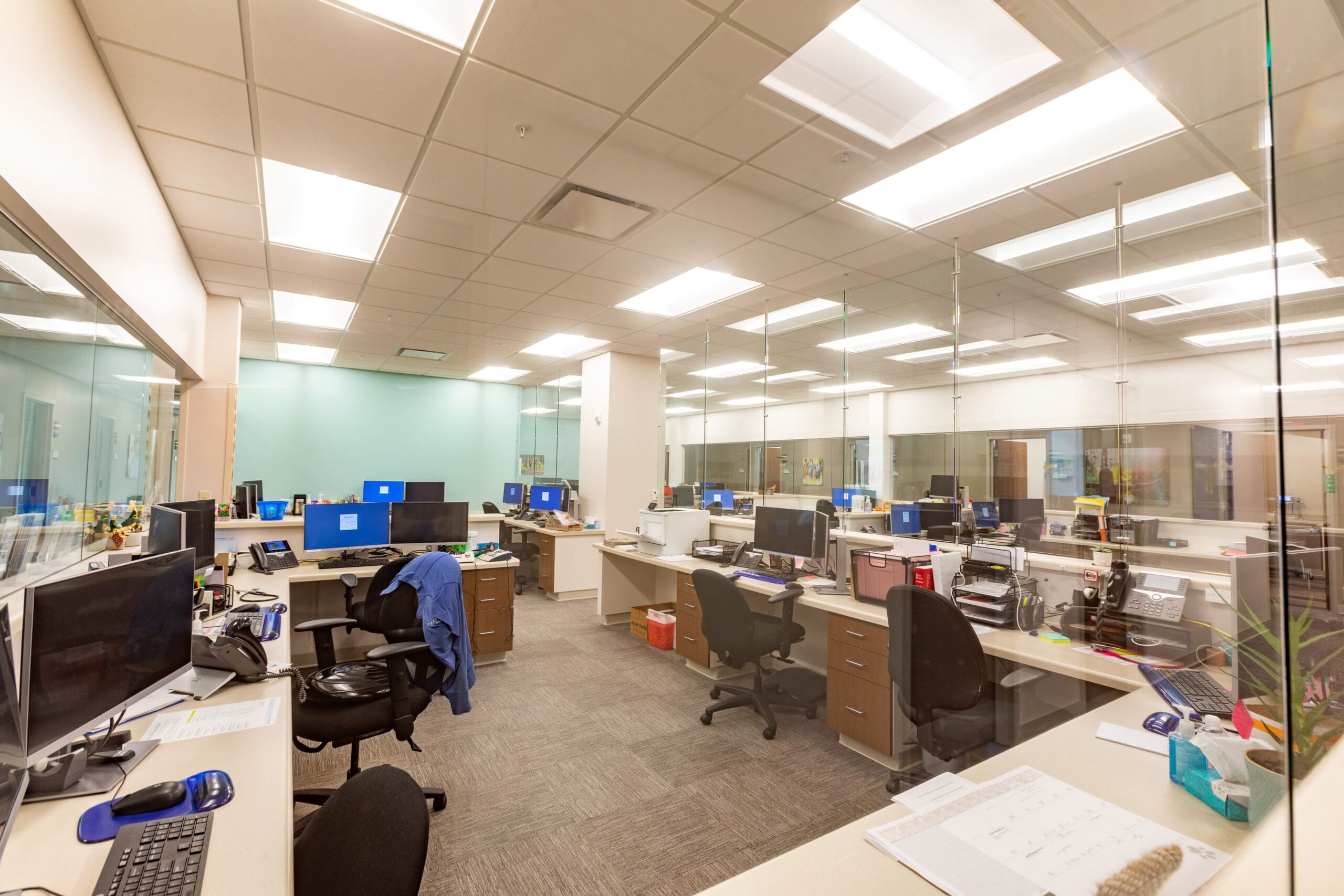 Commercial office space for lease featuring multiple workstations, glass partitions, natural light, and modern furnishings.