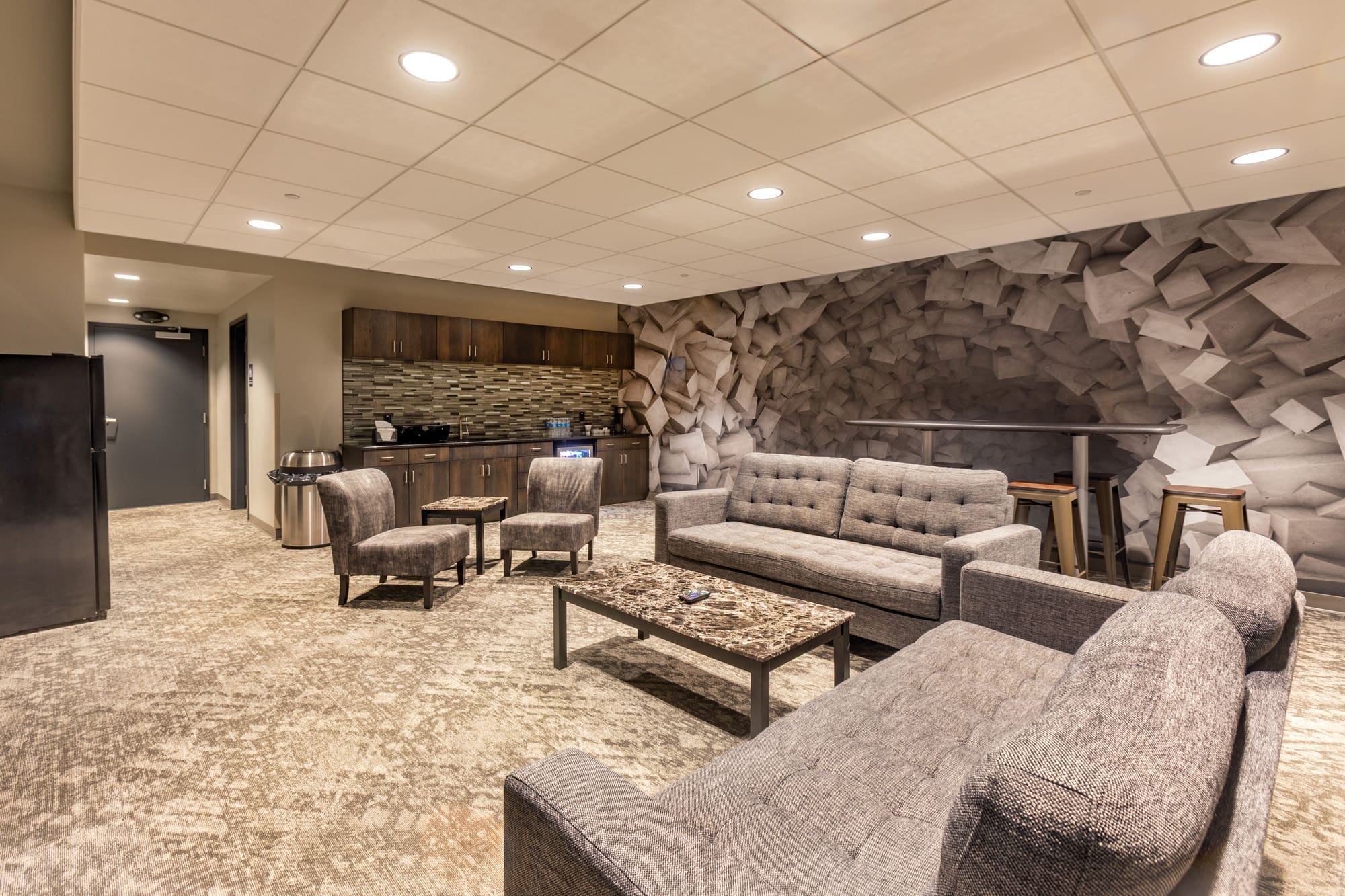 Contemporary residential lounge with gray sofas, marble coffee table, kitchenette, accent wall, and neutral carpet—ideal for real estate.