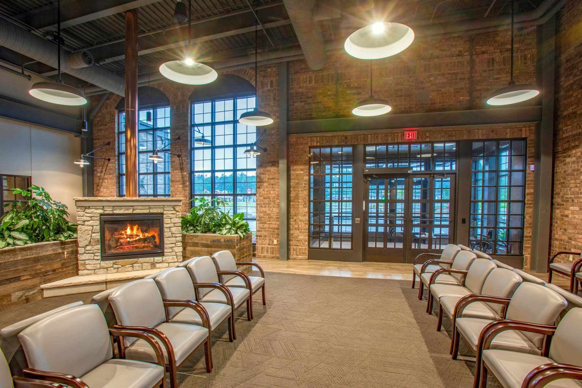 Modern commercial property waiting area with white chairs, stone fireplace, large windows, exposed brick, and designer lighting.