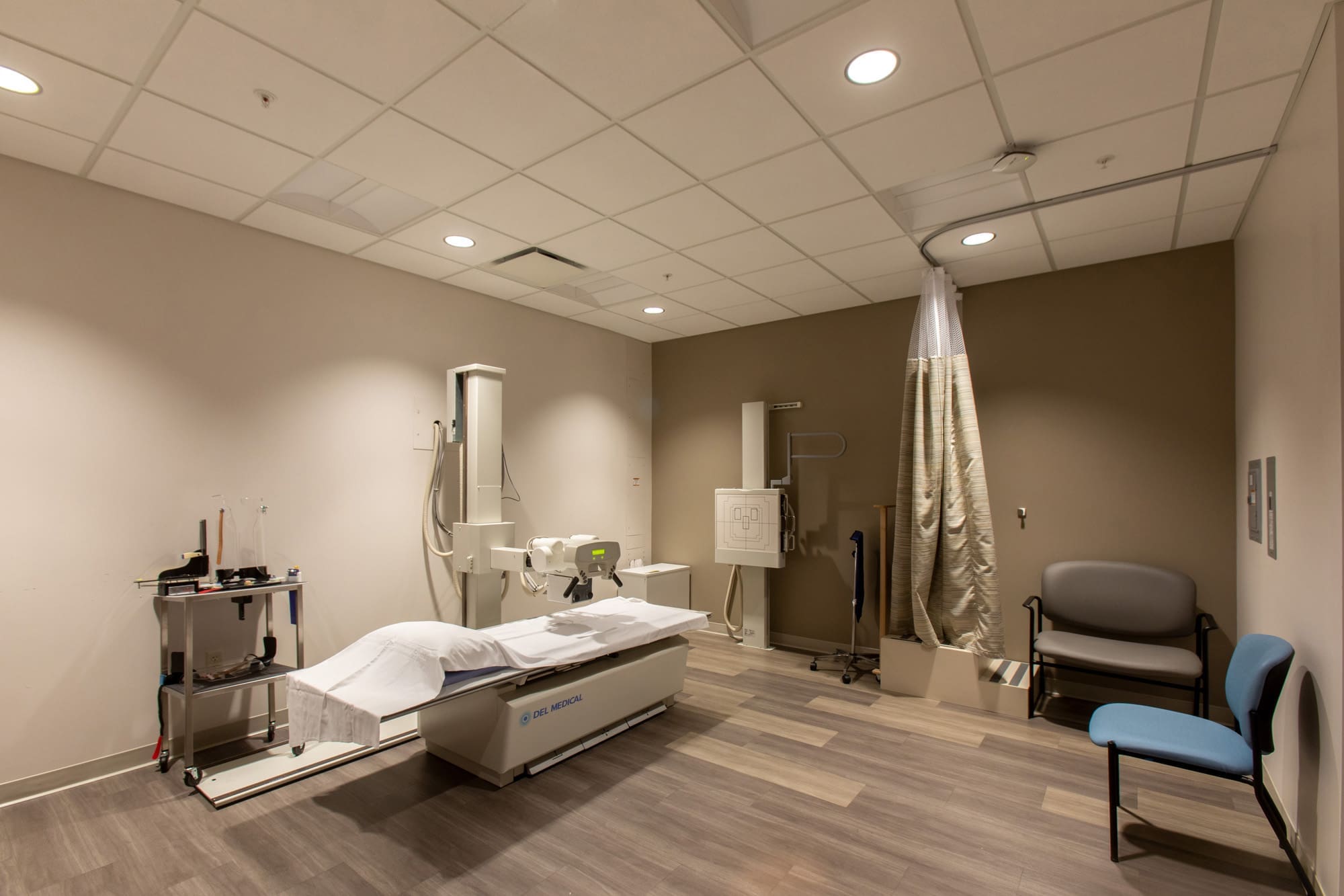 Spacious commercial medical imaging suite featuring an X-ray machine, examination bed, equipment, and seating under bright lighting.