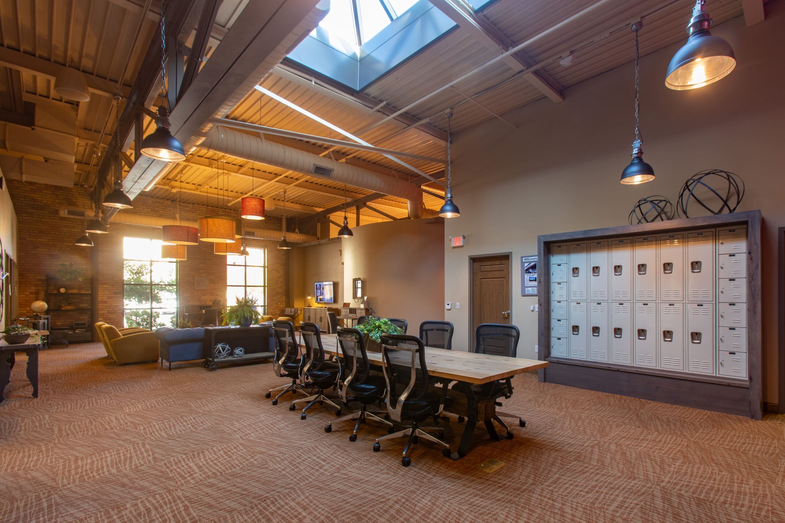 Commercial office space featuring a spacious conference table, sleek black chairs, lockers, lounge seating, large windows, and skylight.